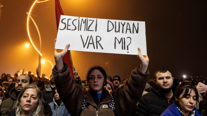 A commemoration held in Hatay, Turkey on the first anniversary of the February 6, 2023 earthquakes. Survivors of the earthquake and families of victims are campaigning for all those responsible for defective buildings to be held accountable. The banner here reads “Is anyone hearing us?” 