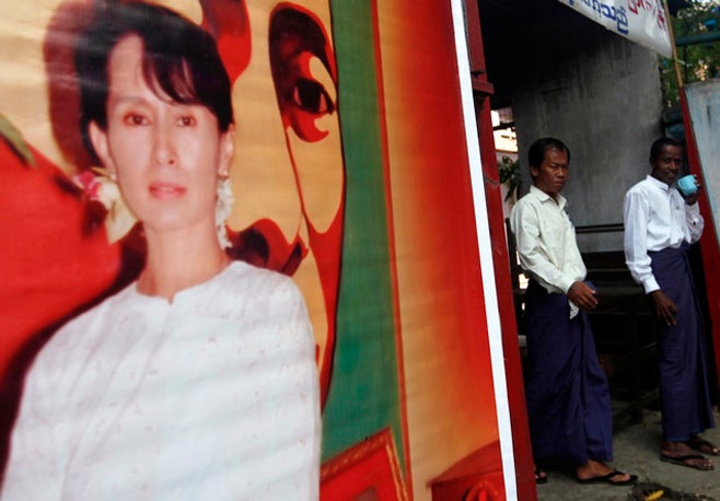 Activists stand behind a poster of Aung San Suu Kyi in front of the office