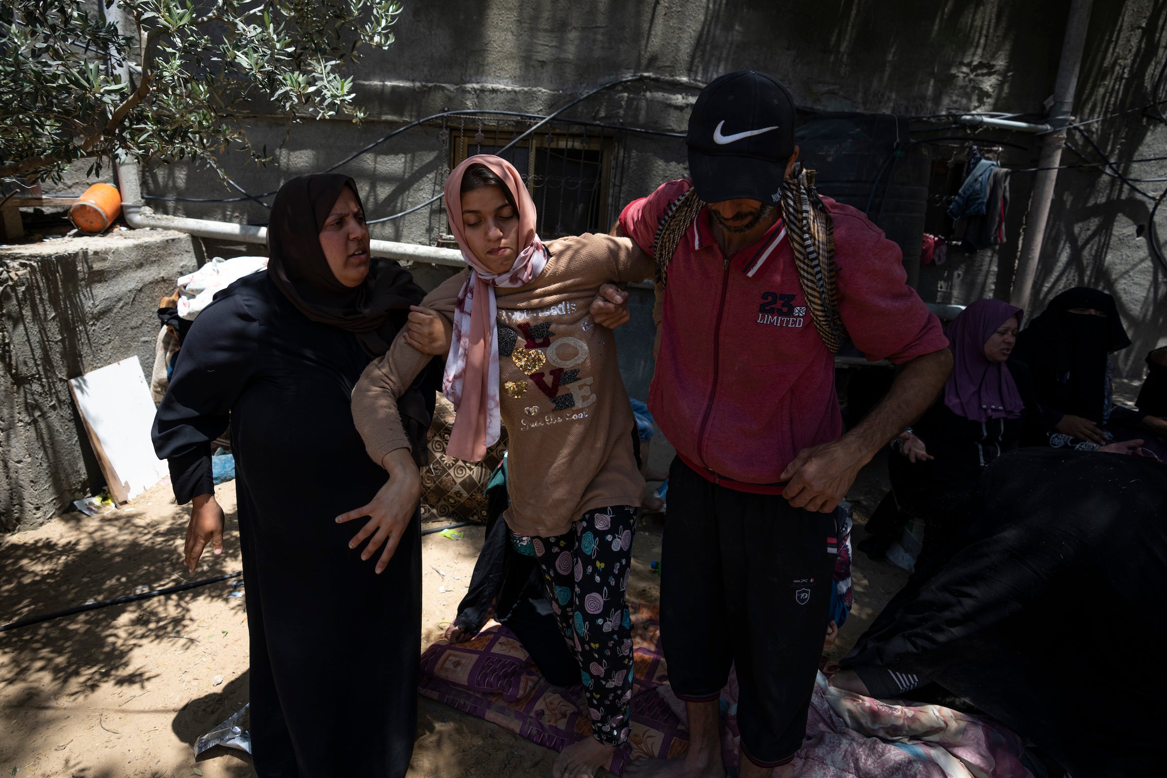 Haneen Nabhan, une jeune femme palestinienne qui a un double handicap physique et intellectuel, soutenue par deux proches près des ruines de la maison de sa famille dans le camp de réfugiés de Jabaliya à Gaza ; cette maison a été détruite lors d'une frappe aérienne israélienne menée le 14 mai 2023. 