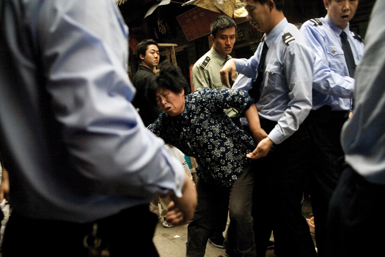 A woman fights with chengguan police as they dismantle part of her small restaurant and confiscate equipment that she stored on the sidewalk outside of her shop in the Fuzi Miao tourist market in central Nanjing, Jiangsu, China. 