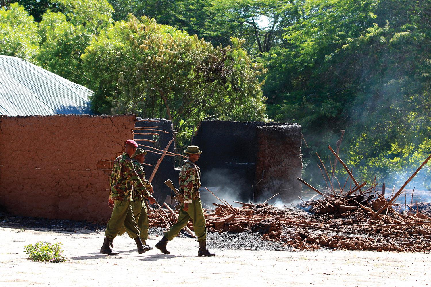 Kenyan police officers walk past the remains of burnt houses after an attack in Kibusu village in Tana River County of the Kenyan Coast on January 10, 2013. Inter-ethnic clashes in 2012 and early 2013 claimed about 180 lives. 