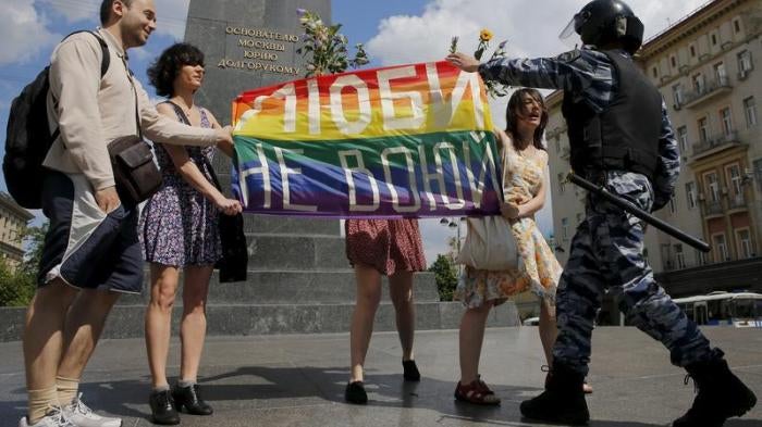Participants in a LGBT community rally in central Moscow, Russia hold a rainbow flag that reads, "Love. Don't make war", as a policeman stops them.