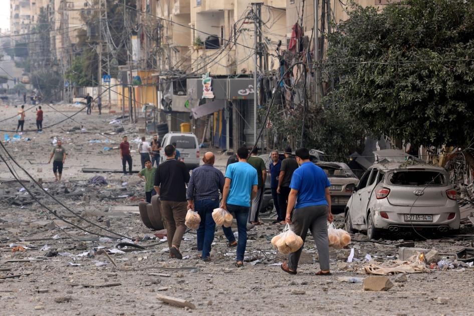 Sejumlah pria Palestina membawa roti di jalan yang rusak parah akibat bom setelah Israel melancarkan serangan udara atas Kota Gaza pada 10 Oktober 2023.