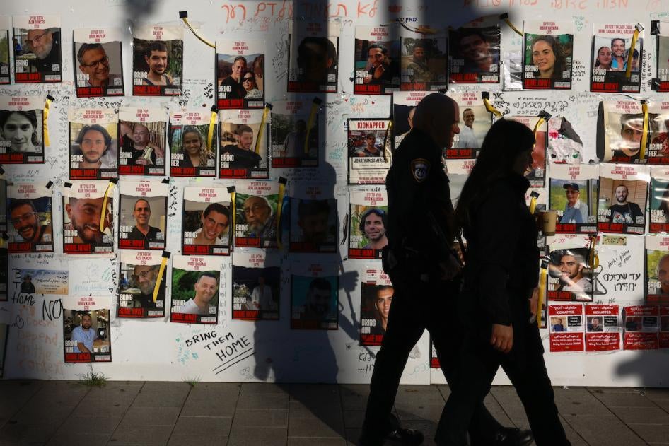 Un policier israélien et une femme marchaient devant un mur ou étaient collées des photos d’otages enlevés le 7 octobre 2023 et détenus à Gaza, dans une rue de Tel Aviv, le 17 décembre 2023.