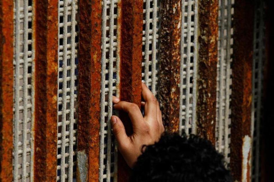 Un hombre, deportado de Estados Unidos hace siete meses, toca las puntas de los dedos de su sobrino a través de la reja que separa México y Estados Unidos.