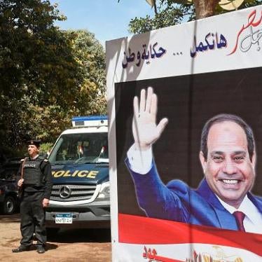 Egyptian policemen standing guard outside a polling station with an electoral banner depicting incumbent President Abdel Fattah al-Sisi seen with a caption reading in Arabic 'for the sake of Egypt we will continue the story of a nation', in the capital Ca