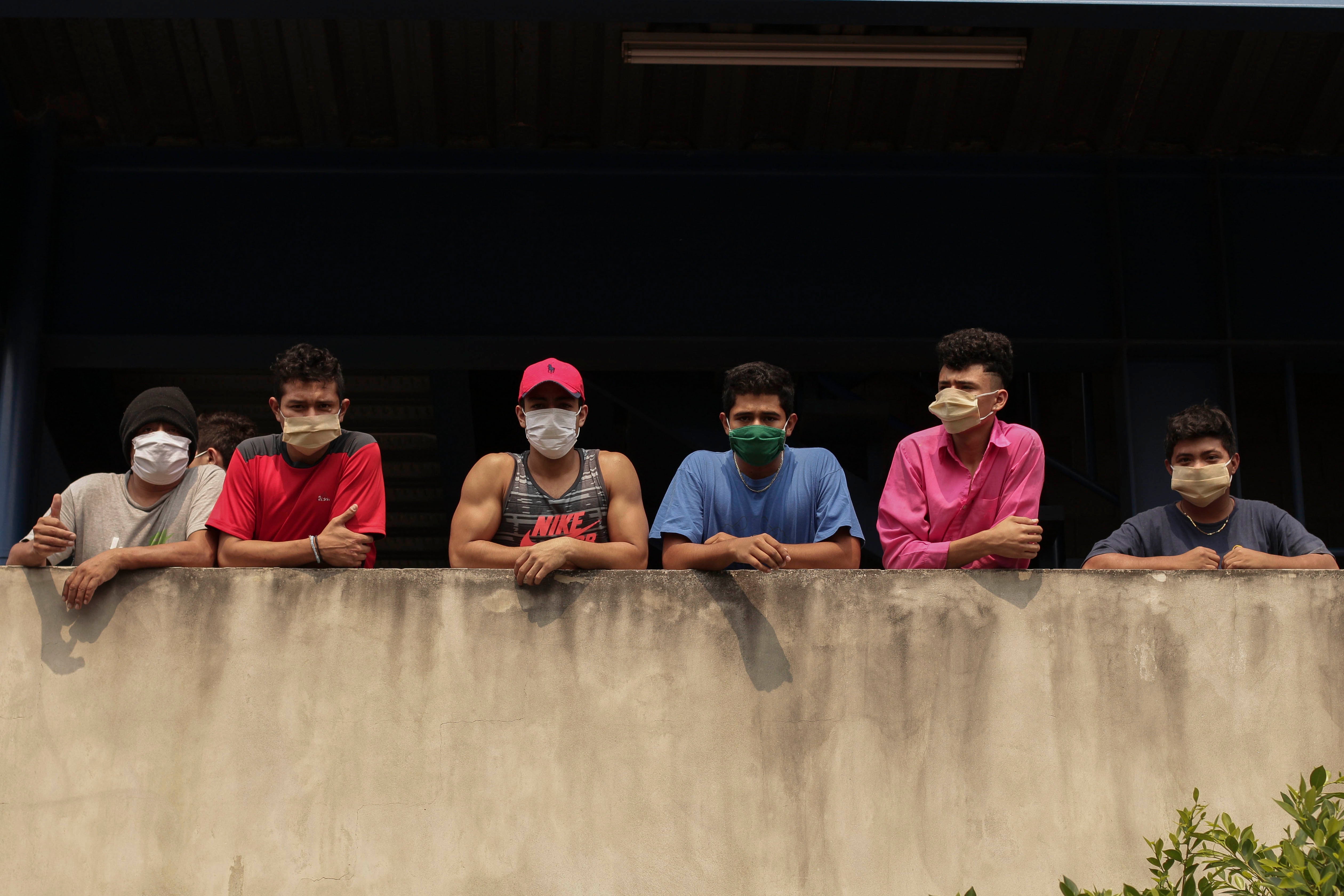 In this May 4, 2020 photo, men wearing protective face masks look out from a building where they are being held for violating a quarantine decreed by the government as part of measures to curb the spread of COVID-19, in San Salvador, El Salvador. 