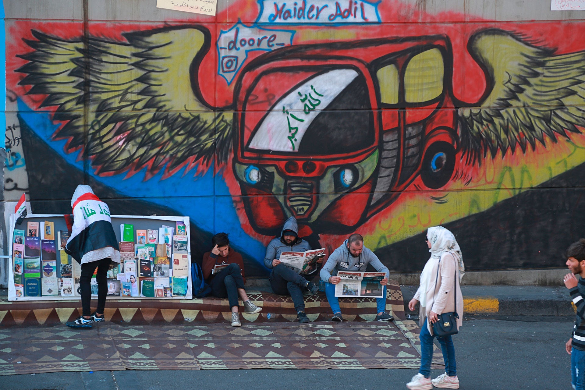 Protesters read copies of newspapers in front of graffiti in Tahrir Square, Baghdad, Iraq, November 20, 2019.