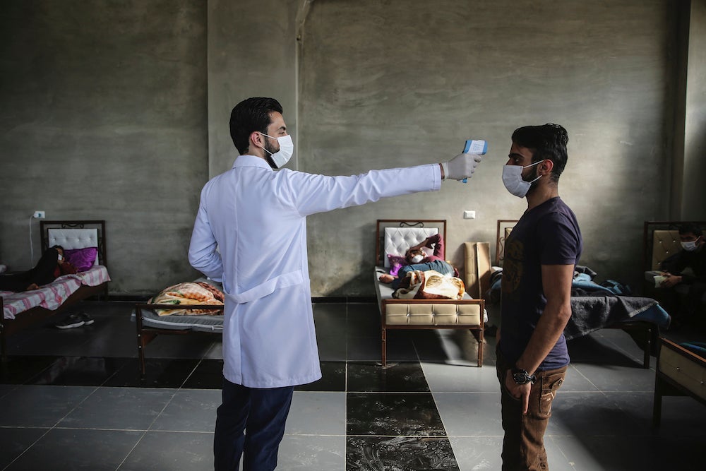 مسعف يقيس حرارة رجل داخل مركز عزل أنشئ على الحدود السورية-التركية لإيداع الناس القادمين من تركيا إلى إدلب كإجراء وقائي ضد انتشار فيروس كورونا. 