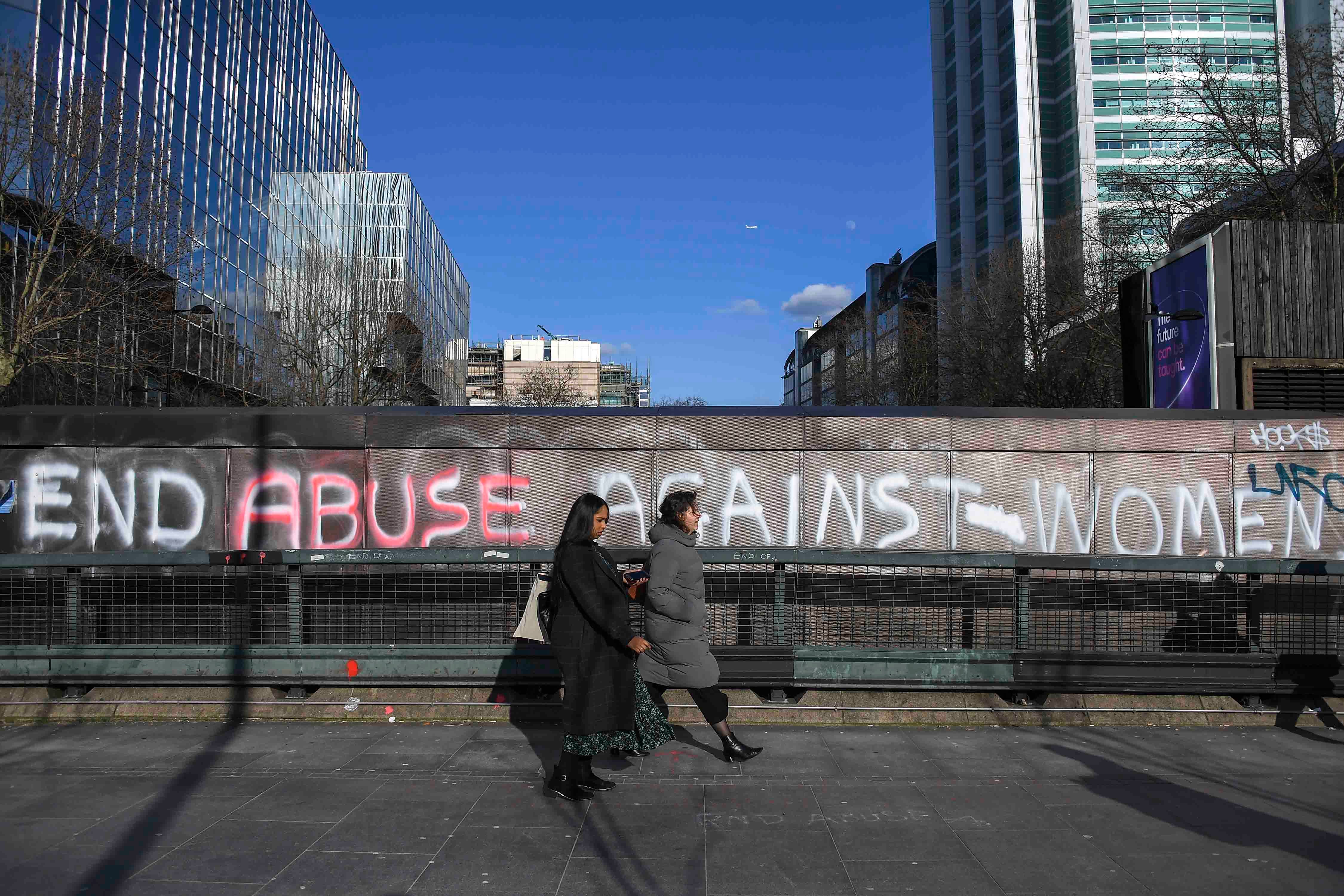 عبارة "أوقفوا العنف ضد النساء" مكتوبة على جدار في شارع يوستون في لندن، وتظهر في الصورة امرأتان تمران بجانب الجدار، الجمعة 6 مارس/آذار 2020. 
