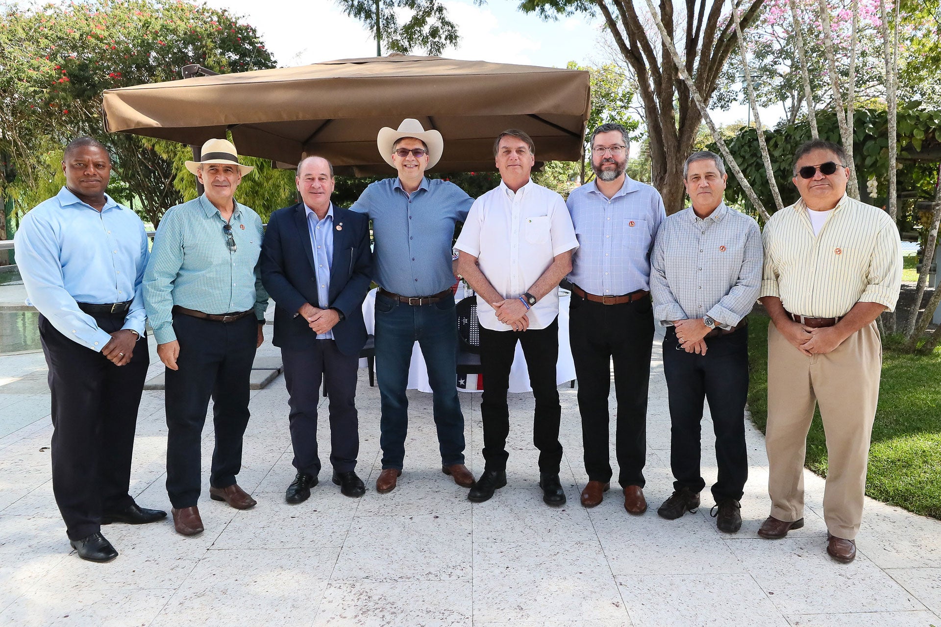 Brazil´s President Jair Bolsonaro (center, wearing a white shirt) poses for a picture with US Ambassador Todd Chapman (center, wearing a hat) and several ministers during a luncheon at the ambassador´s residence, July 4, 2020.