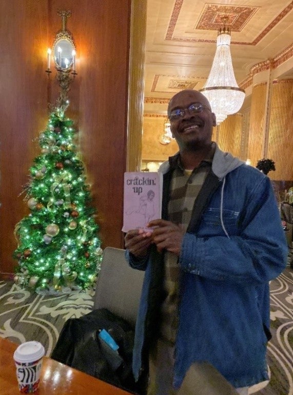 A man poses with a novel in front of a Christmas tree