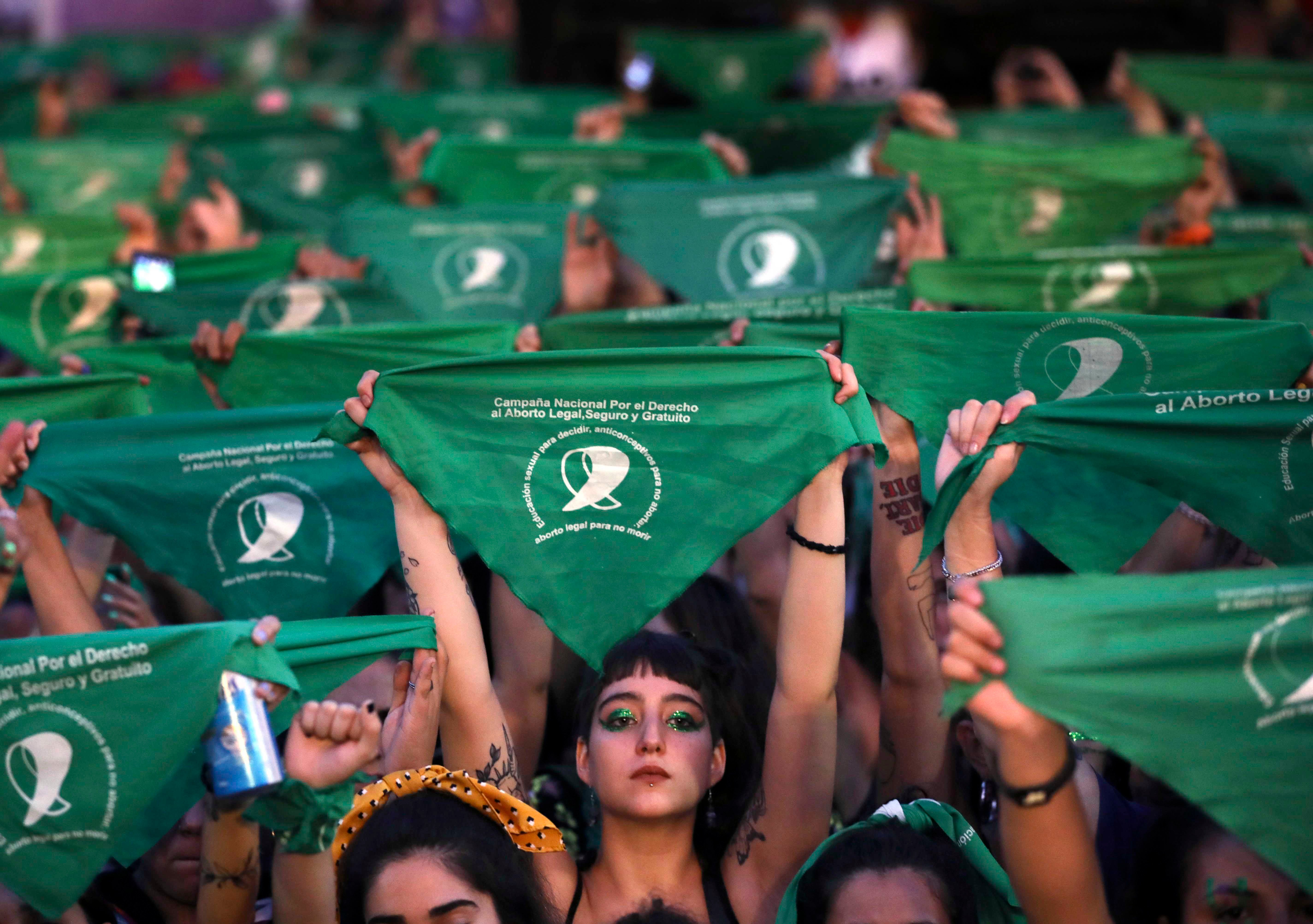 A crowd of women hold up green protest signs