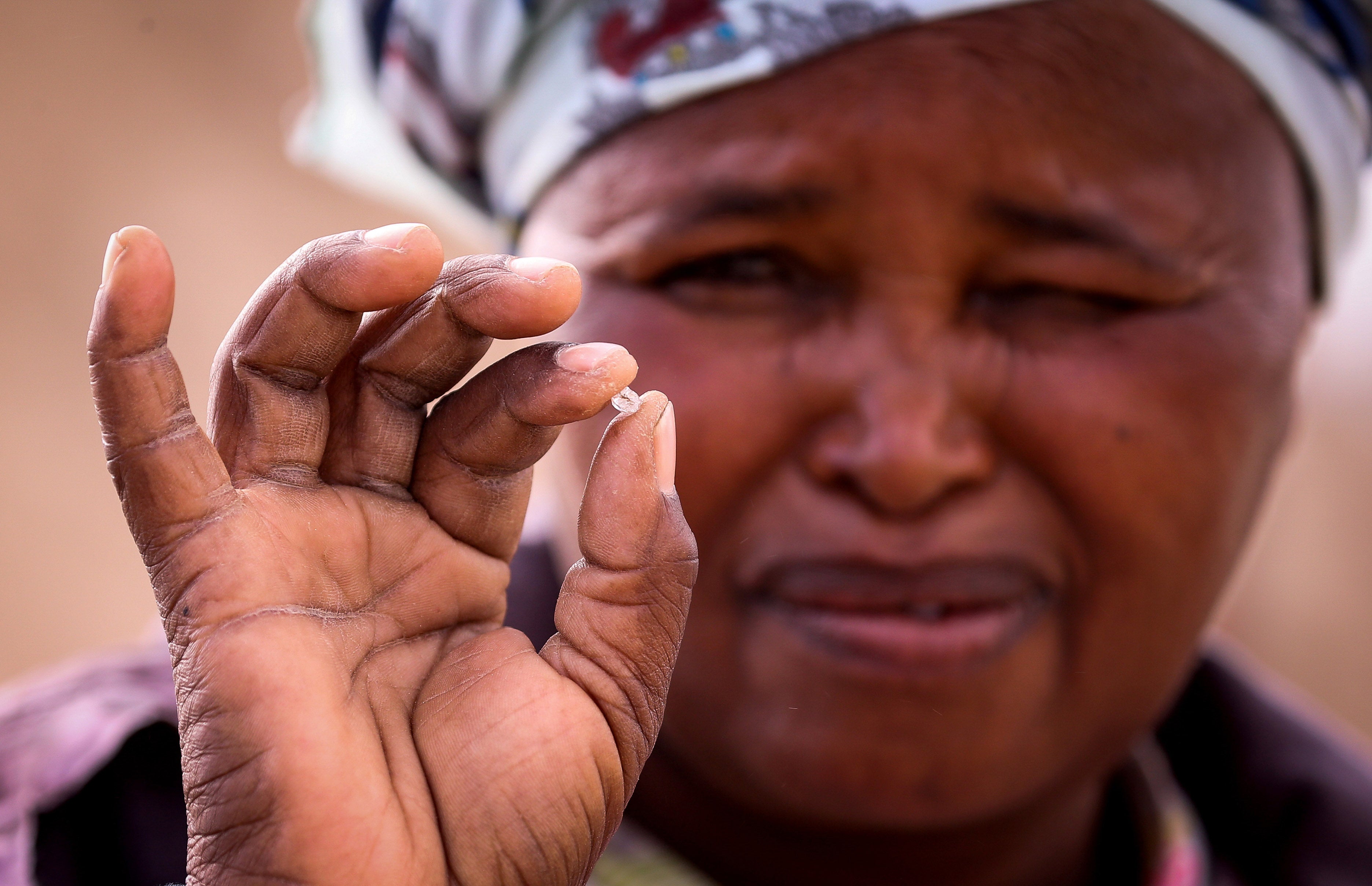 A woman squints while holding a small diamond in her fingers