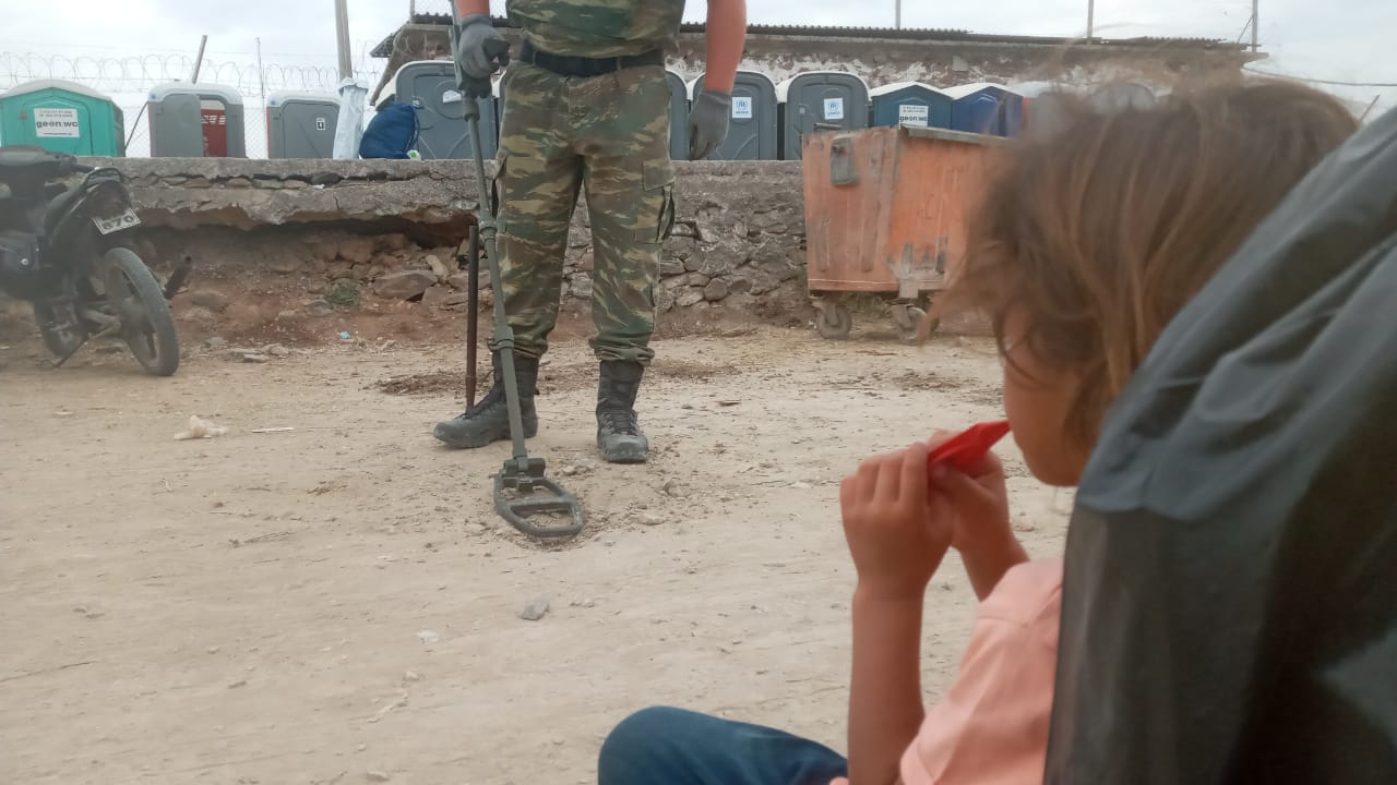 A girl from Syria living in Mavrovouni camp watches the Greek military search for unexploded munitions