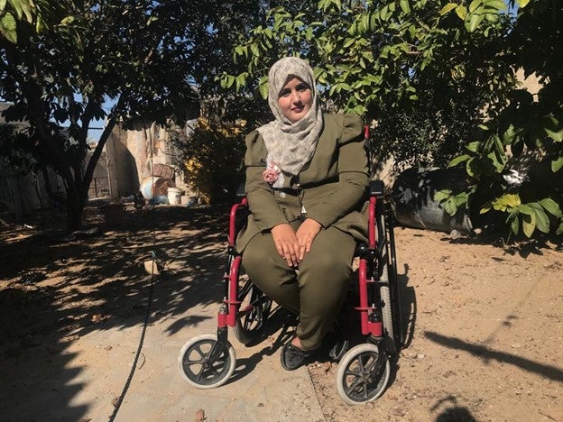 Abeer Qashlan, a 24-year-old a woman with a physical disability who uses a wheelchair and a mobility scooter, at the yard of her home in Gaza.