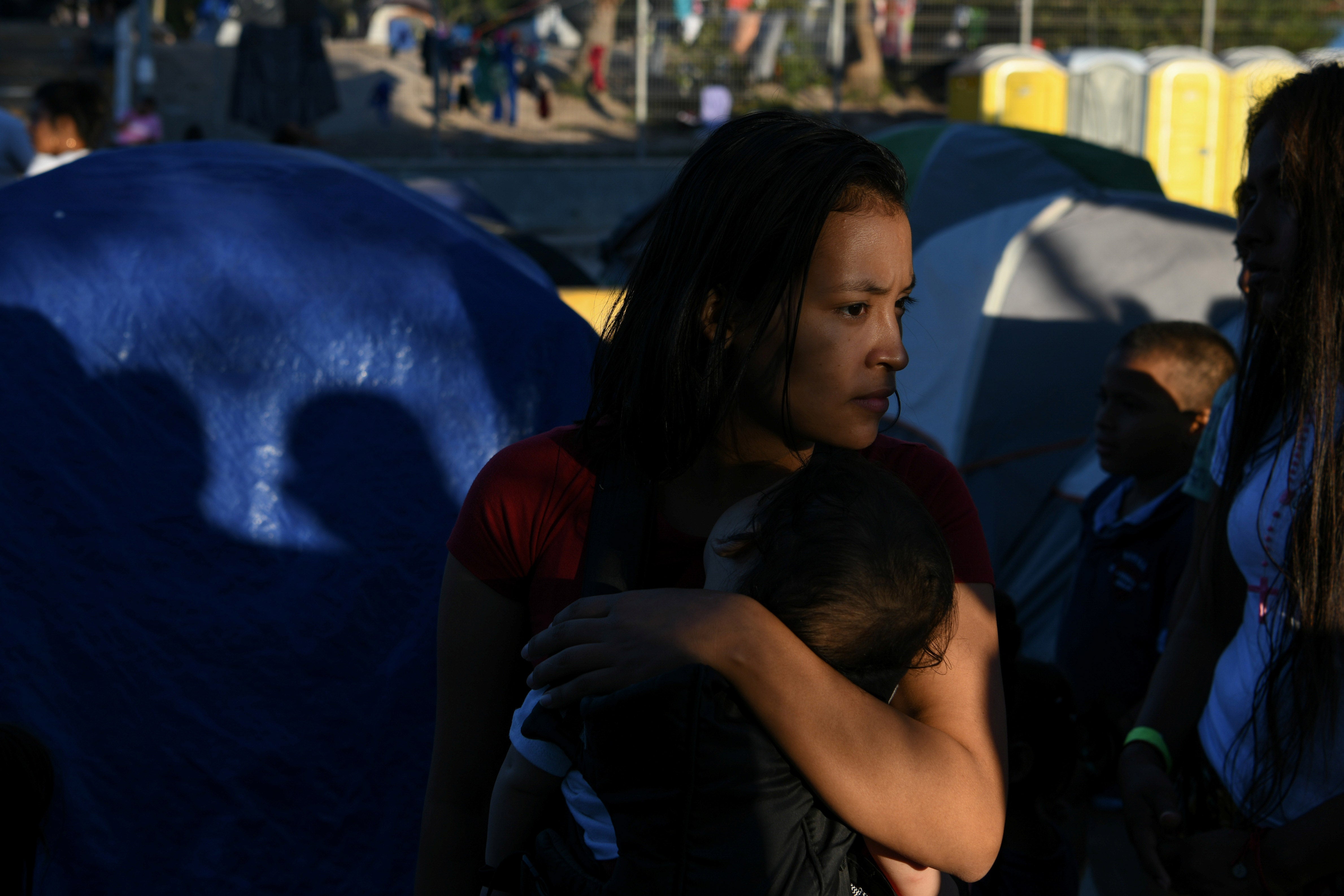 A woman holds a child in front of a group of tents