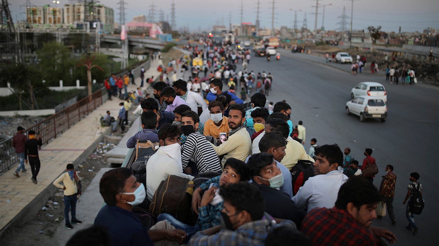 Indian migrant workers sit atop a bus as others walk along an expressway to return to their home villages during a nationwide Covid-19 lockdown, New Delhi, India, March 28, 2020.