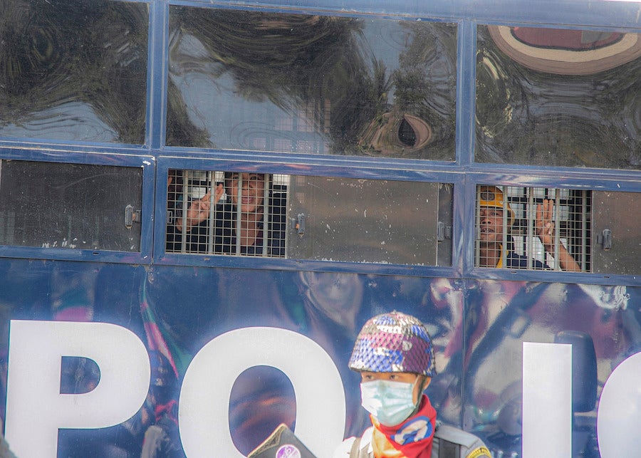 Deux manifestants aperçus derrière les barreaux des petites fenêtres d’un véhicule de police à Mandalay, au Myanmar, le 9 février 2021. Leur salut à trois doigts symbolise leur opposition au coup d’État du 1er février. 