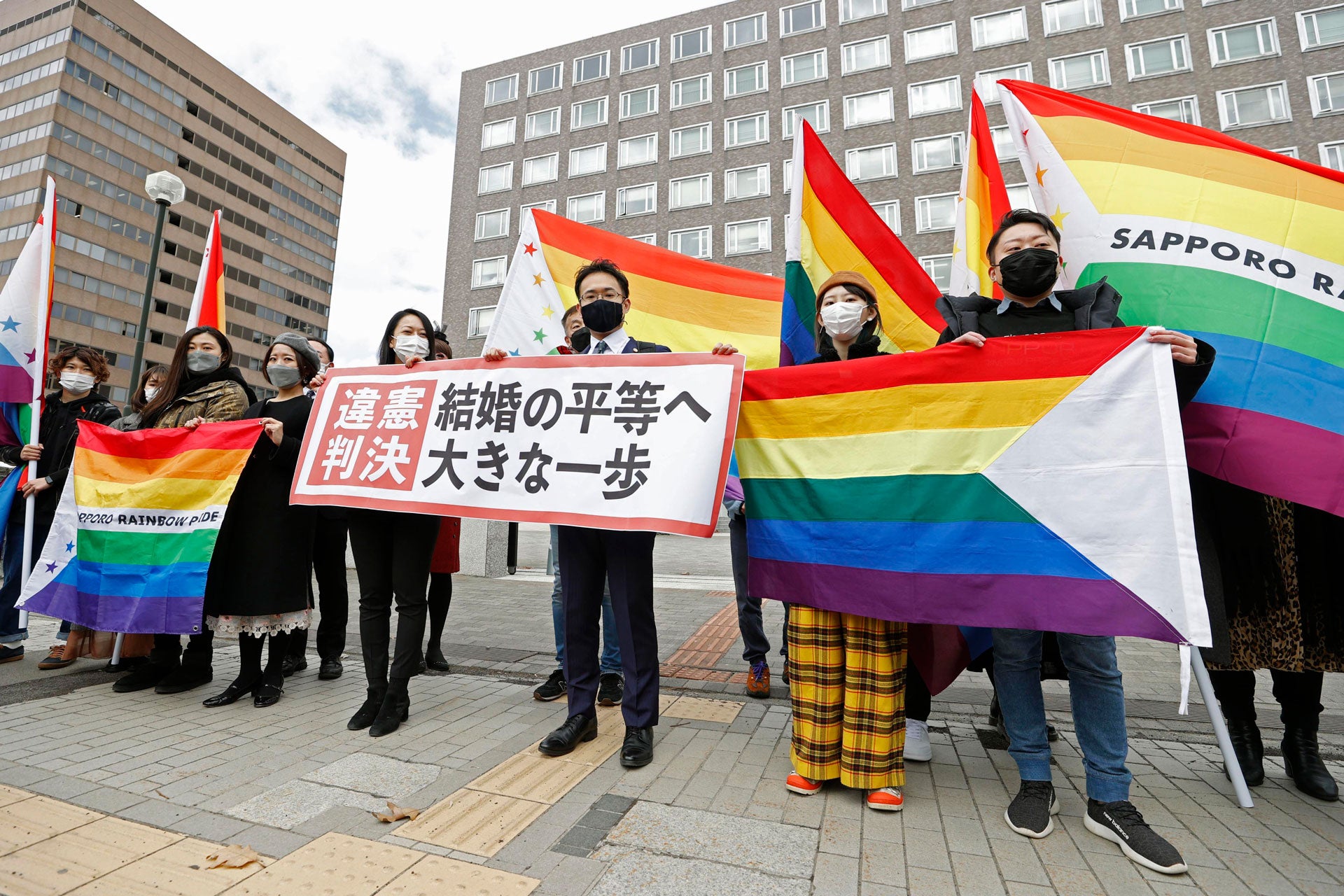 Lawyers and supporters hold rainbow flags and a banner outside Sapporo District Court in Sapporo, Japan, March 17, 2021. 