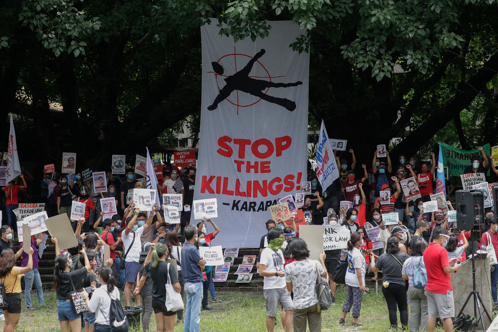 Protesters hold signs during a rally in front of a giant banner that reads, "Stop The Killings."