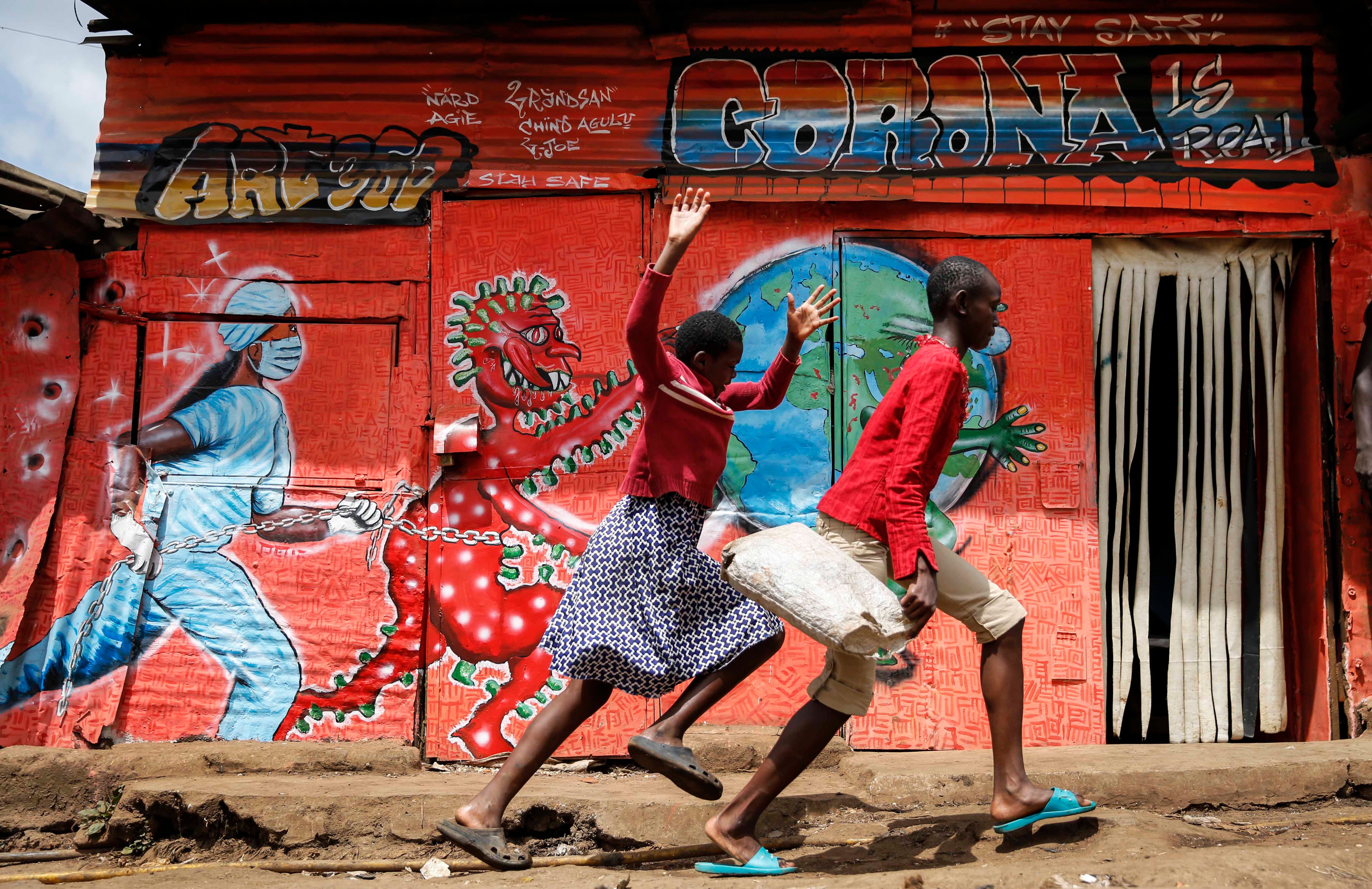 Children run past a mural that warns people about the dangers of the new coronavirus, in the Kibera informal settlement of Nairobi, Kenya.