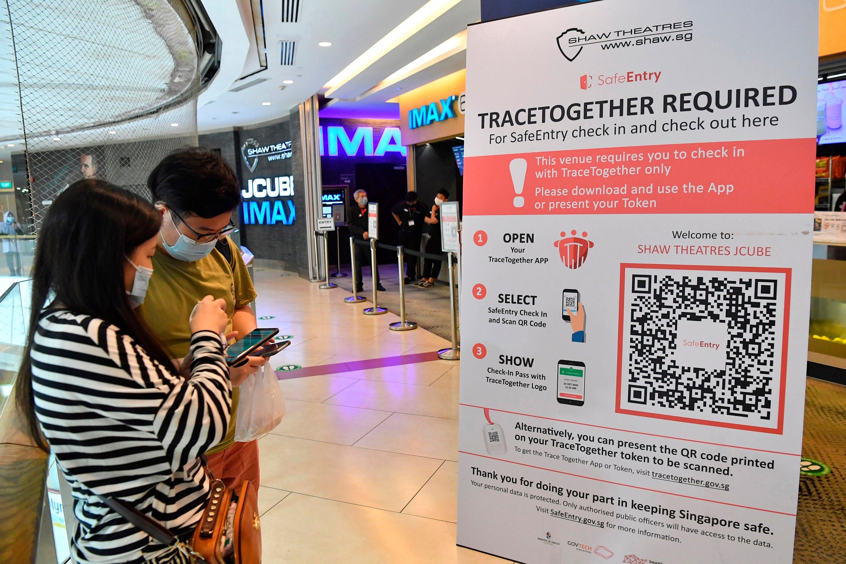 Cinemagoers downloading the TraceTogether app on their mobile phones to check in before entering Shaw Theatres at JCube mall in Singapore, October 31, 2020.