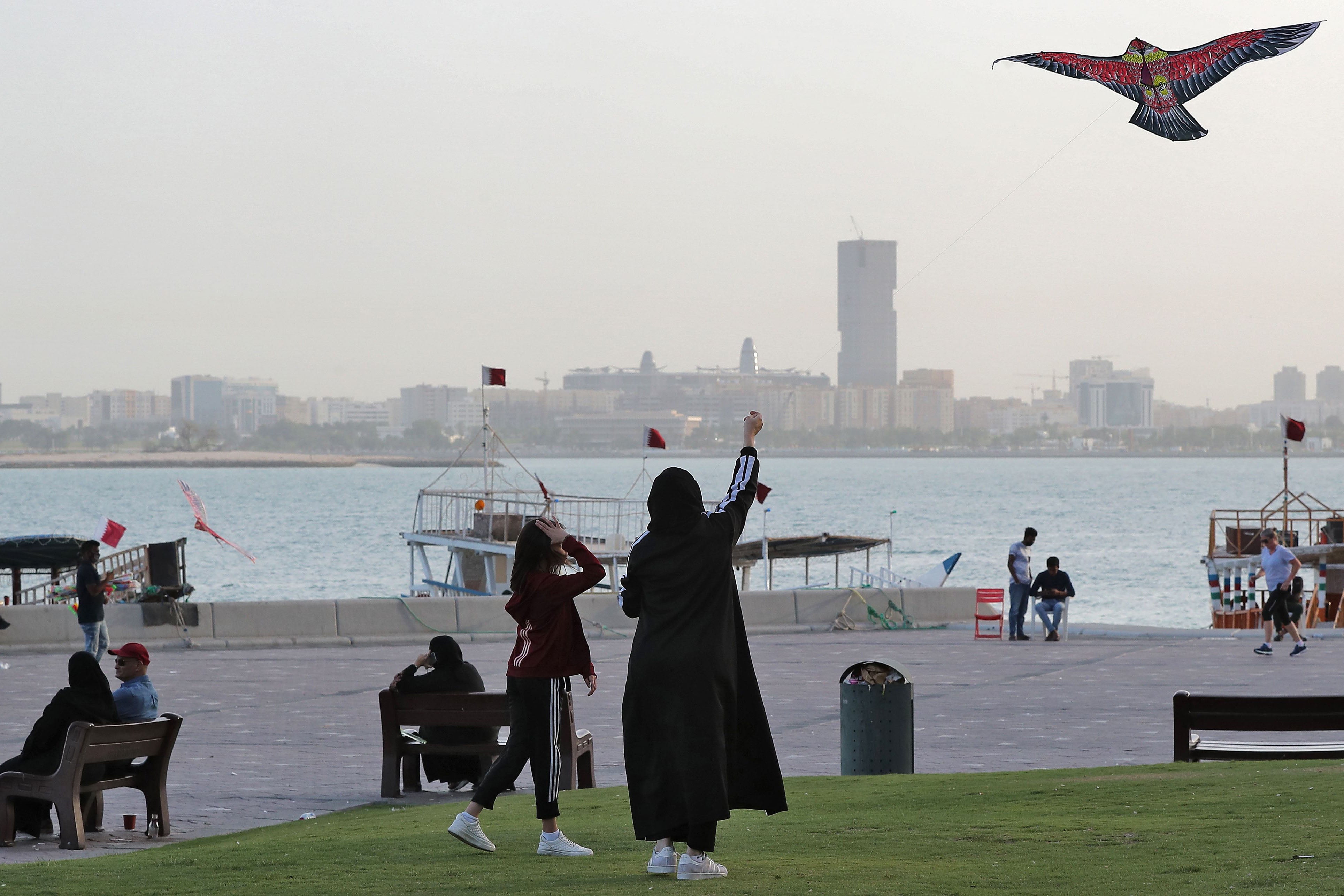 Women fly a kite in a park next to a body of water