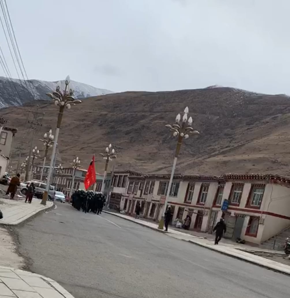 Screenshot of a video showing dozens of police and commandos parading through the town of Dza Wonpo, carrying a large red flag and shouting battle-cries.
