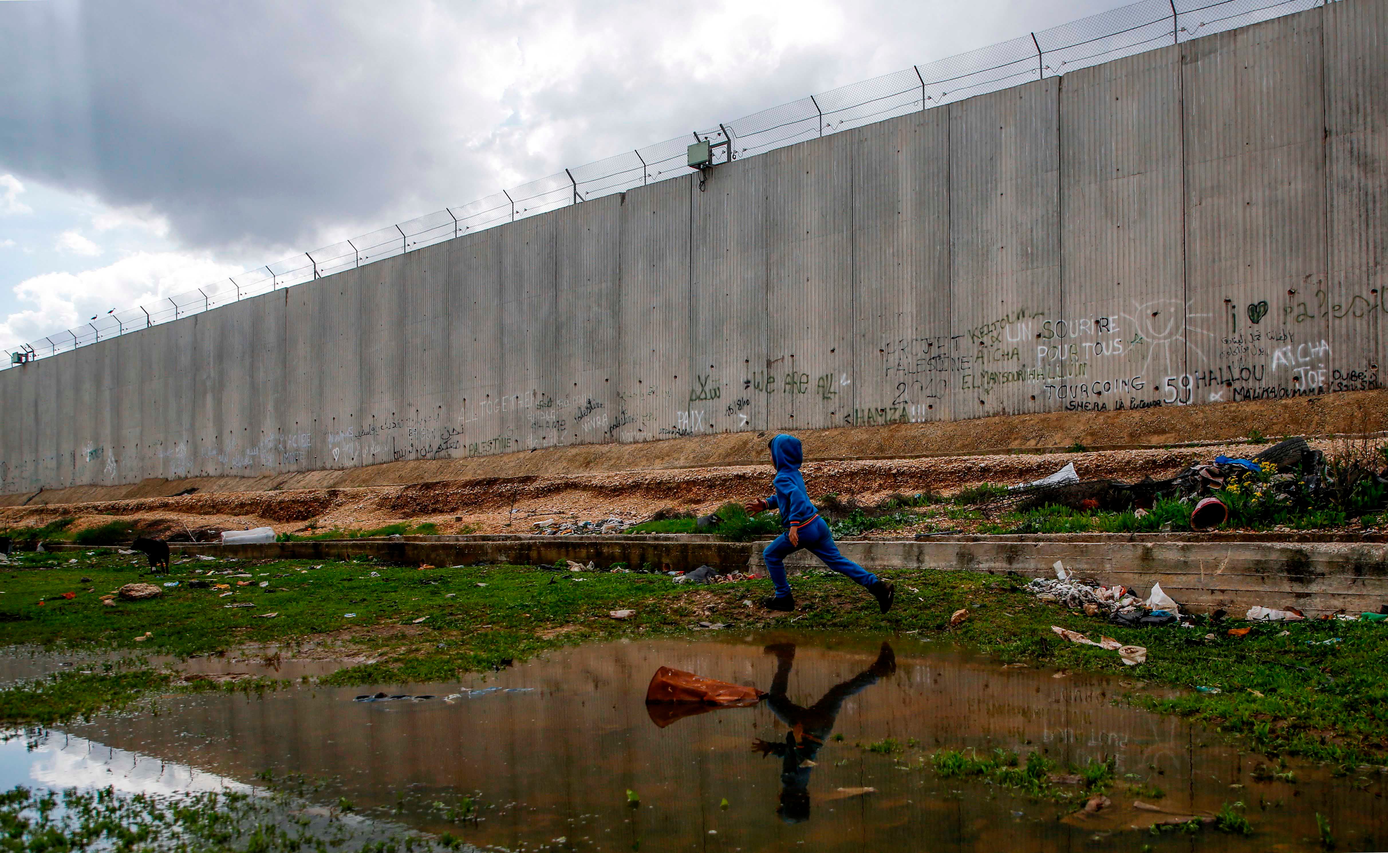 A boy runs alongside a tall concrete wall