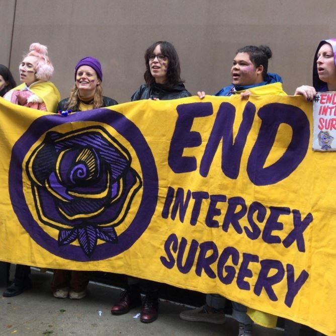 People hold a yellow banner reading "End Intersex Surgeries" in purple writing
