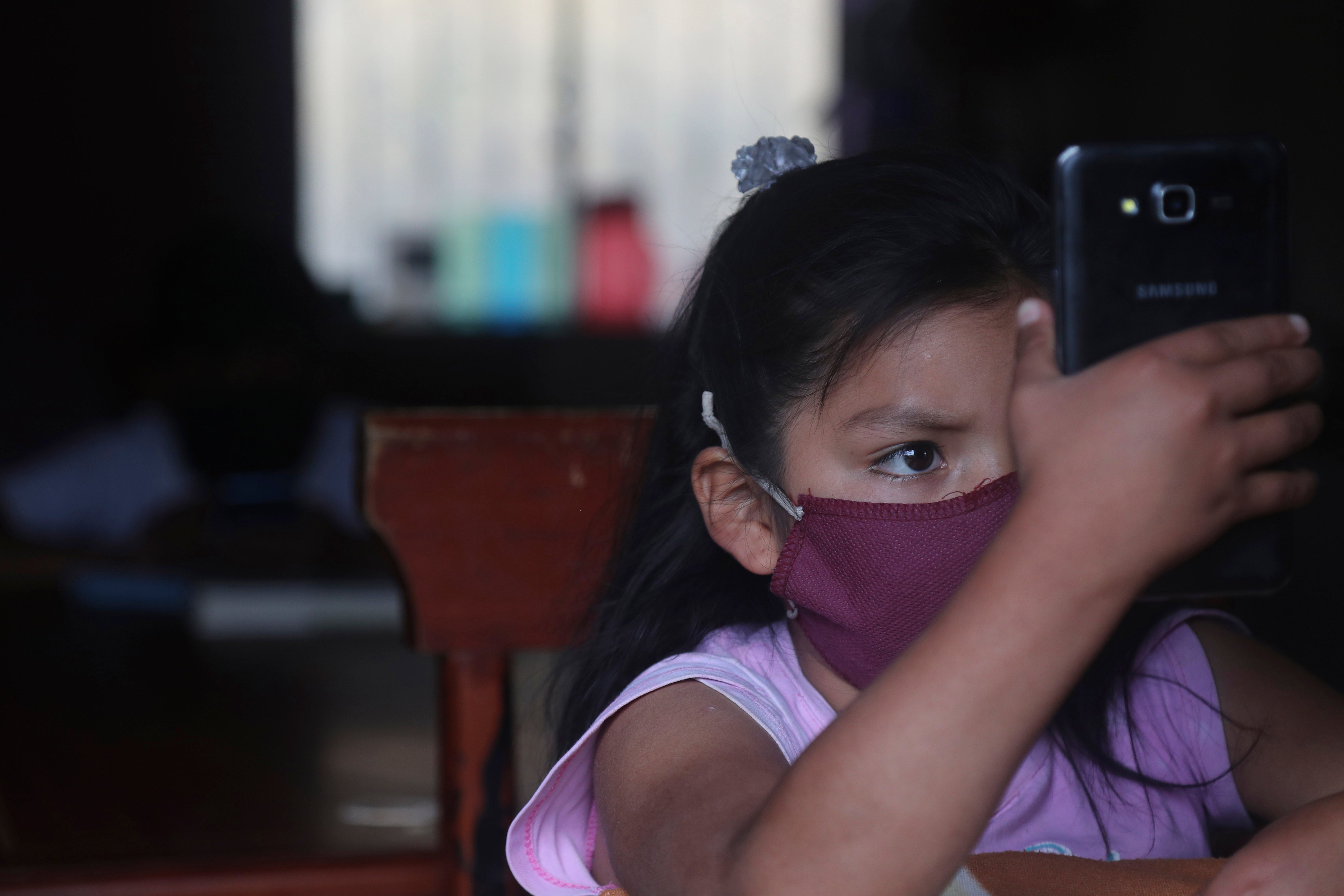 A young girl wearing a face mask holds up a cell phone