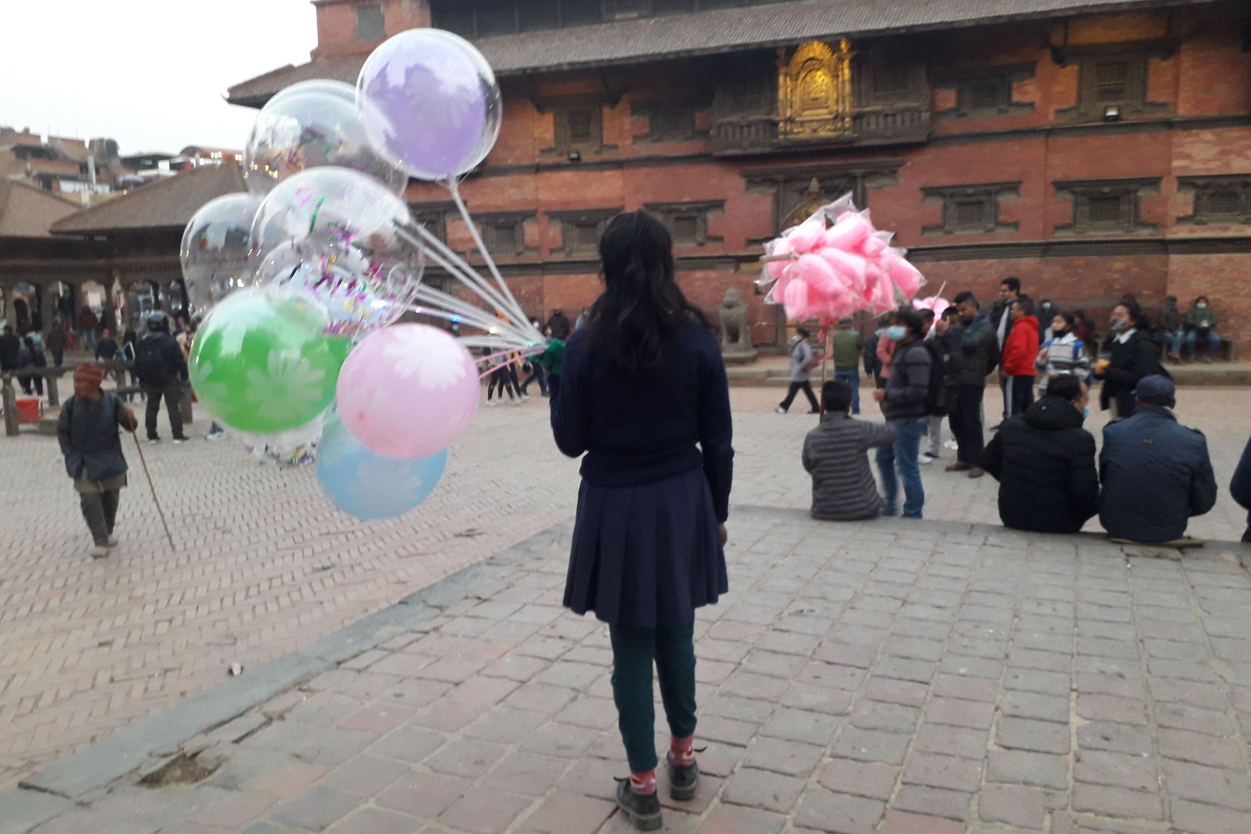 A girl holds a group of balloons to sell in a town square