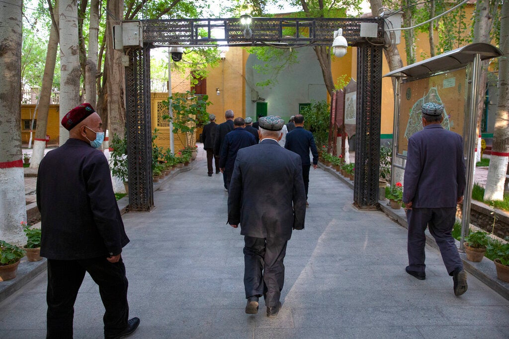 Uyghur Muslims walk under an arch with security cameras after prayers at the Id Kah Mosque in Kashgar in China's Xinjiang region, during a government-organized trip for foreign journalists, April 19, 2021.