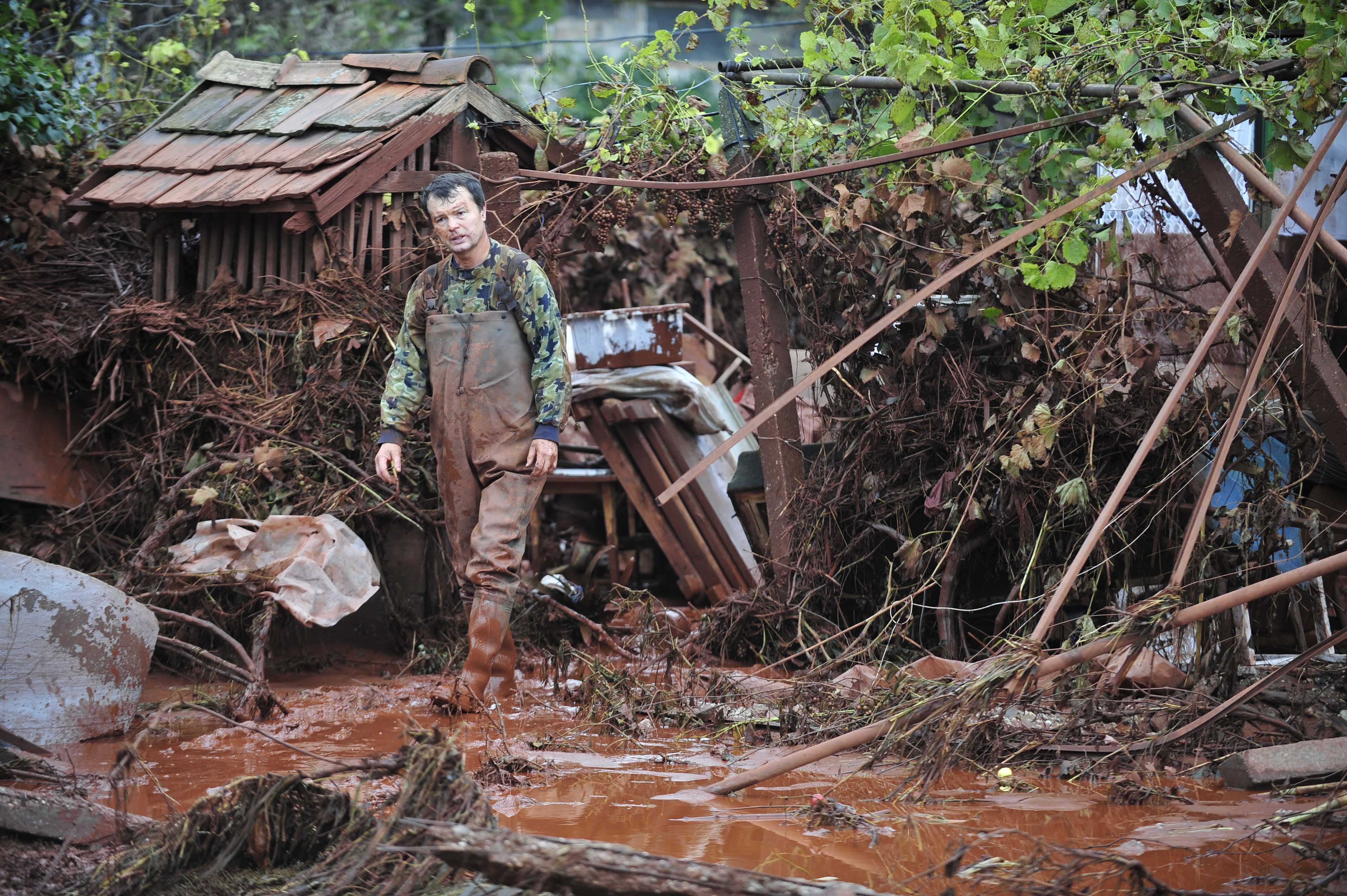 A man walking in mud outside a partially destroyed home