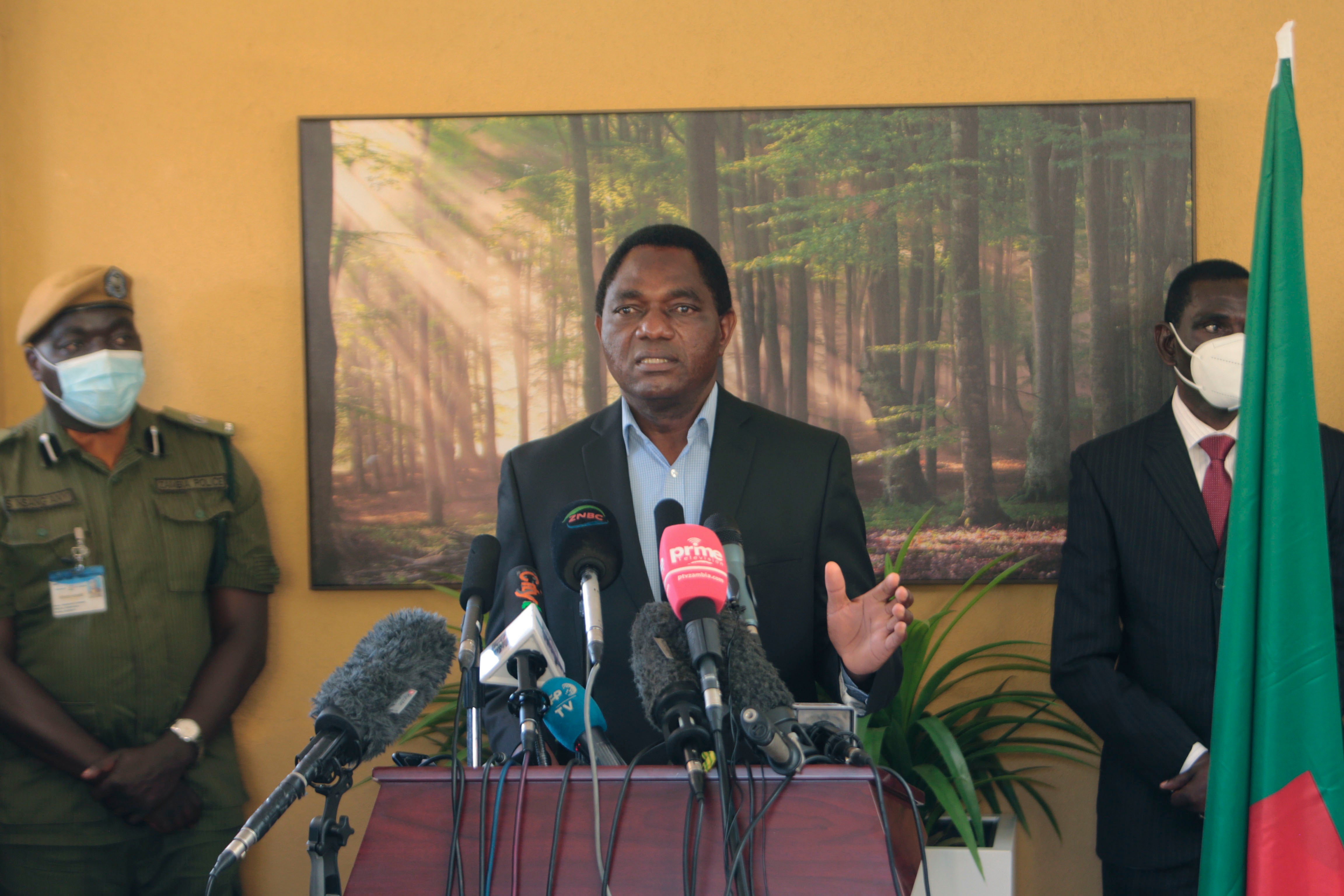 A man stands at a podium flanked by two people in face masks