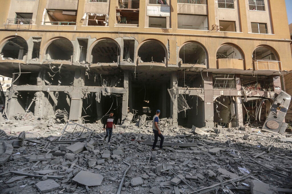 People in Gaza stand in the debris near the site of the severely damaged al-Jawhara tower 