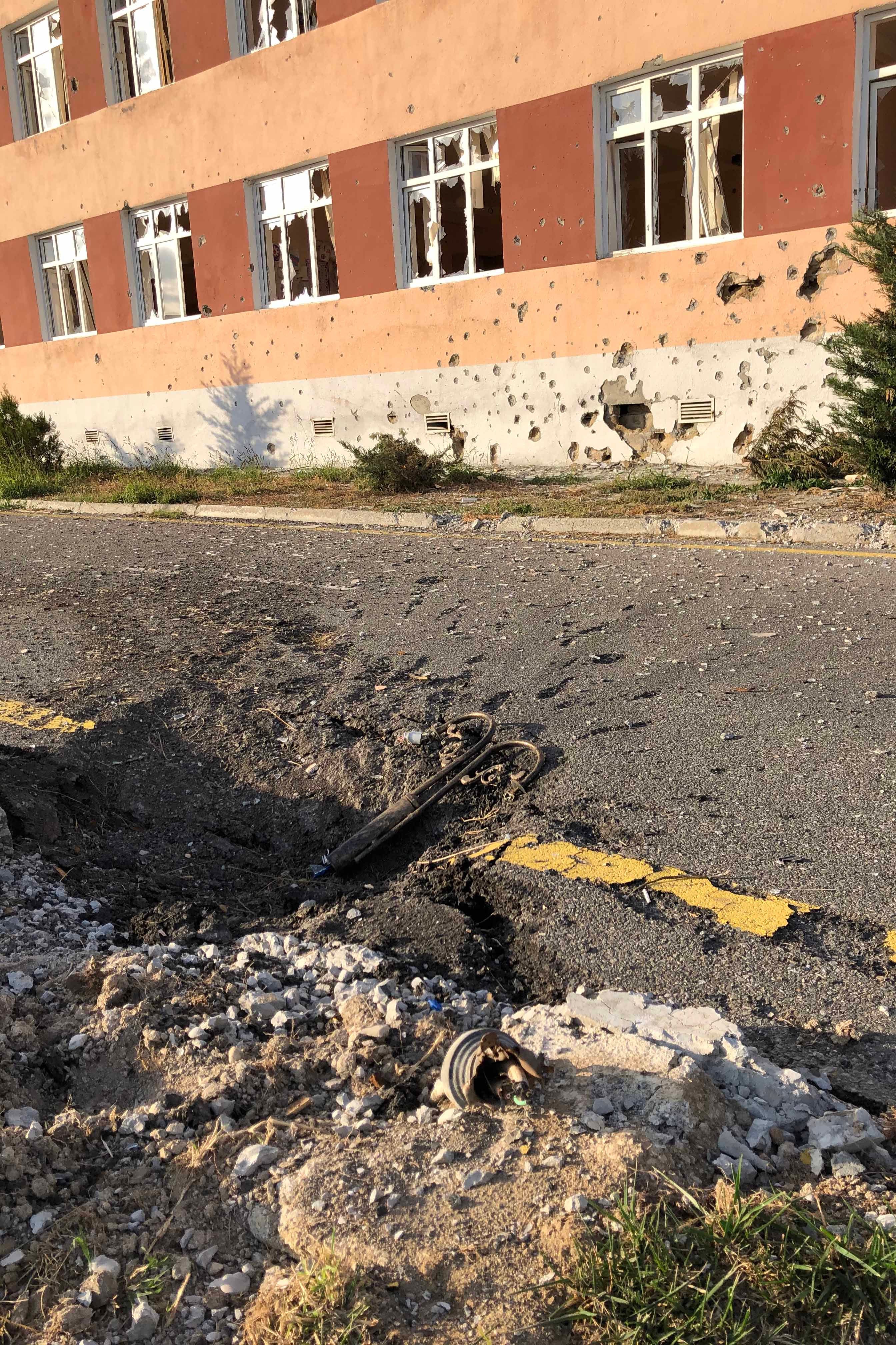 A missile crater in a paved road and shelling damage to the exterior of a school