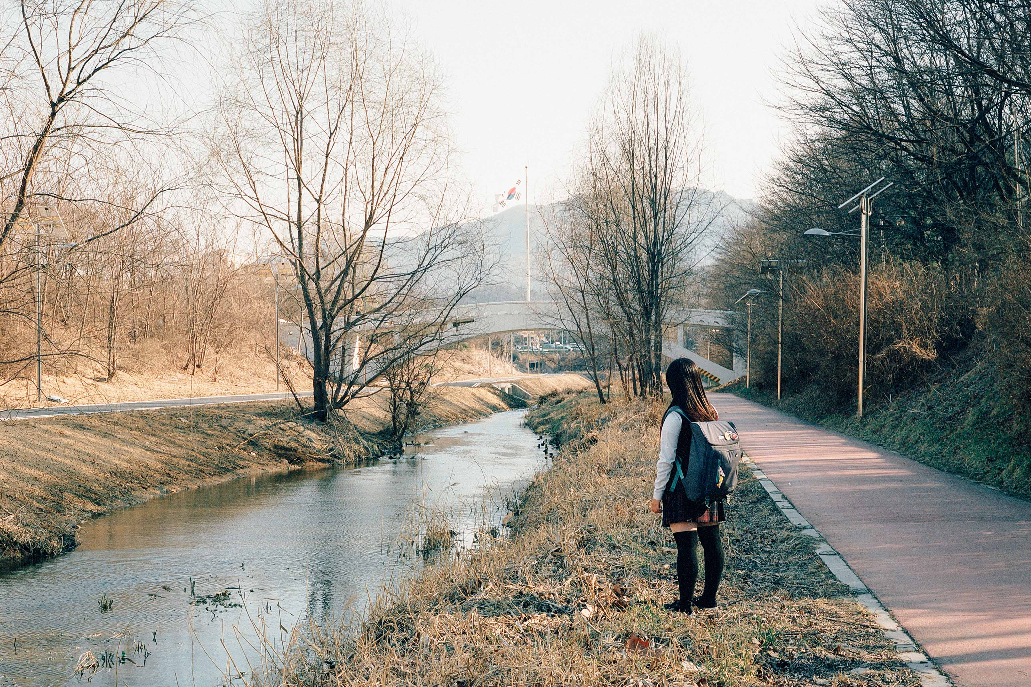 A schoolgirl stands next to a stream 