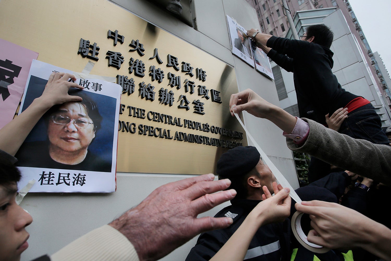 抗議人士在香港中聯辦門口張貼桂民海（圖左，本名桂敏海）及其他香港銅鑼灣書店失蹤人員的相片，2016年1月3日。