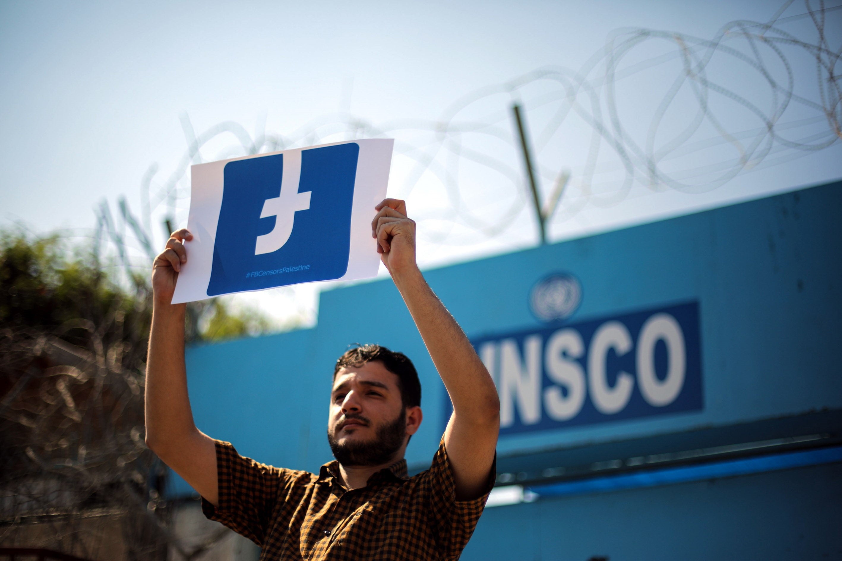 A Palestinian demonstrator holds a banner of the Facebook logo.