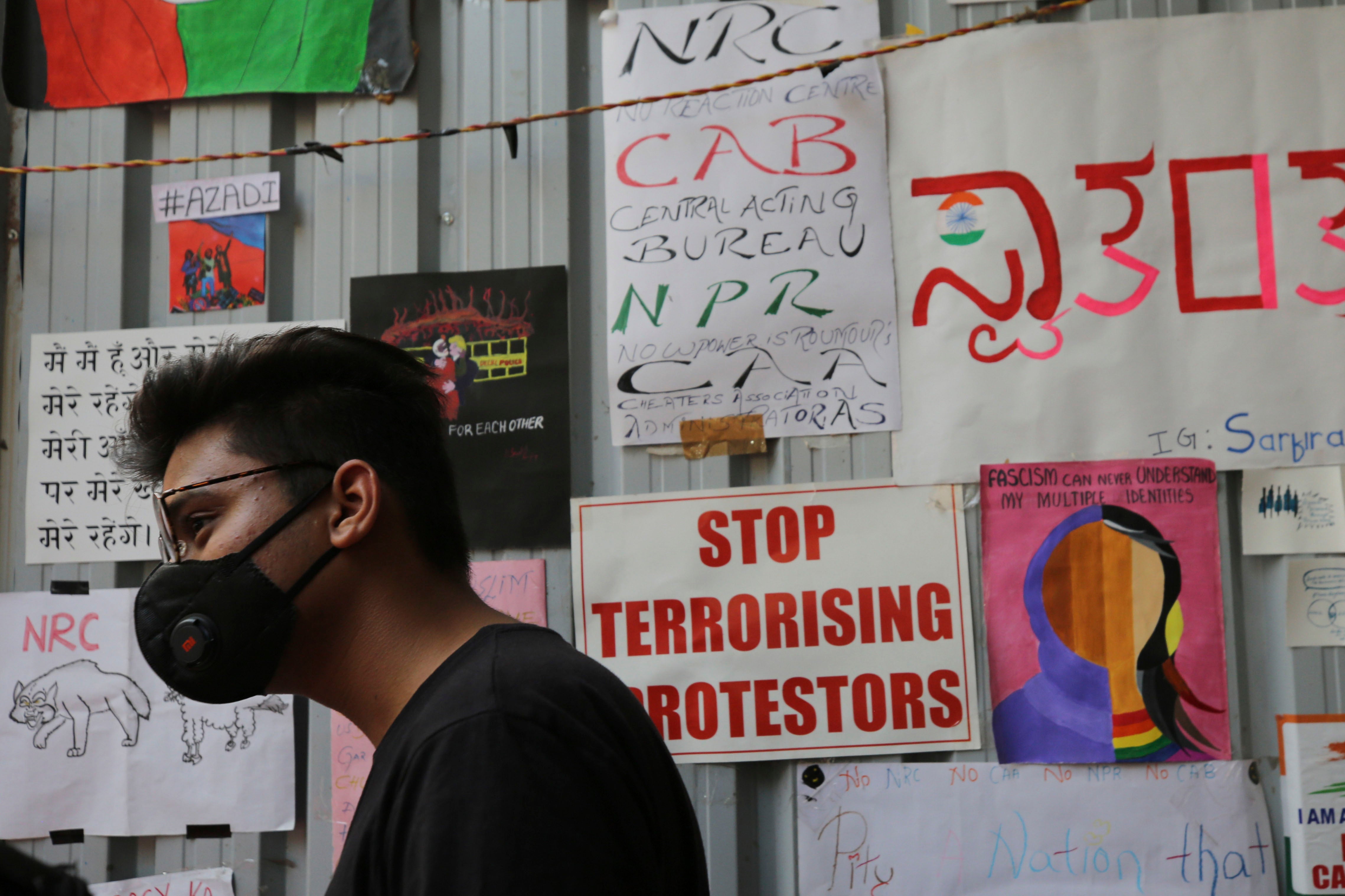 A man in a face mask stands in front of a variety of protest placards