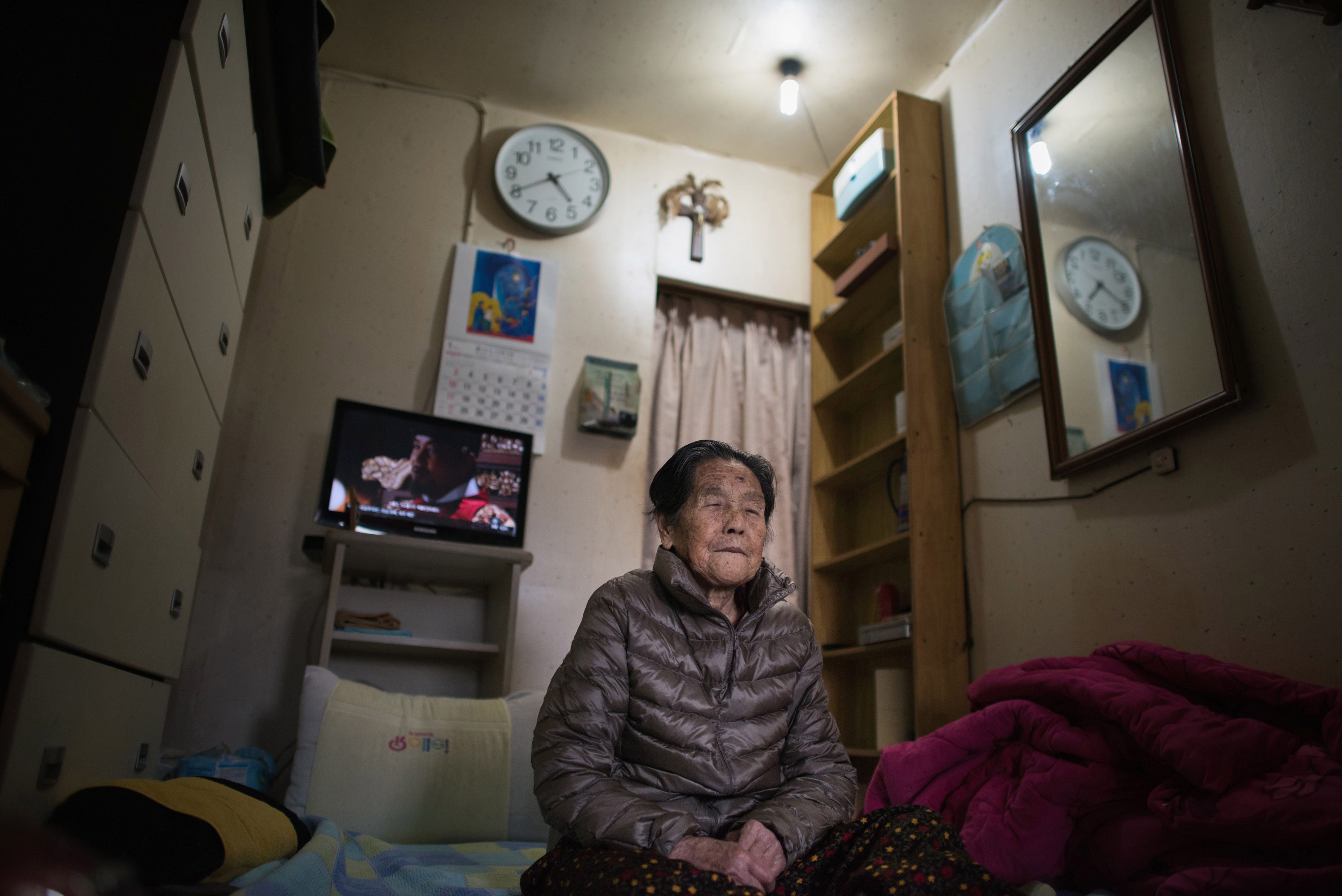 An elderly woman seated on the floor of an apartment