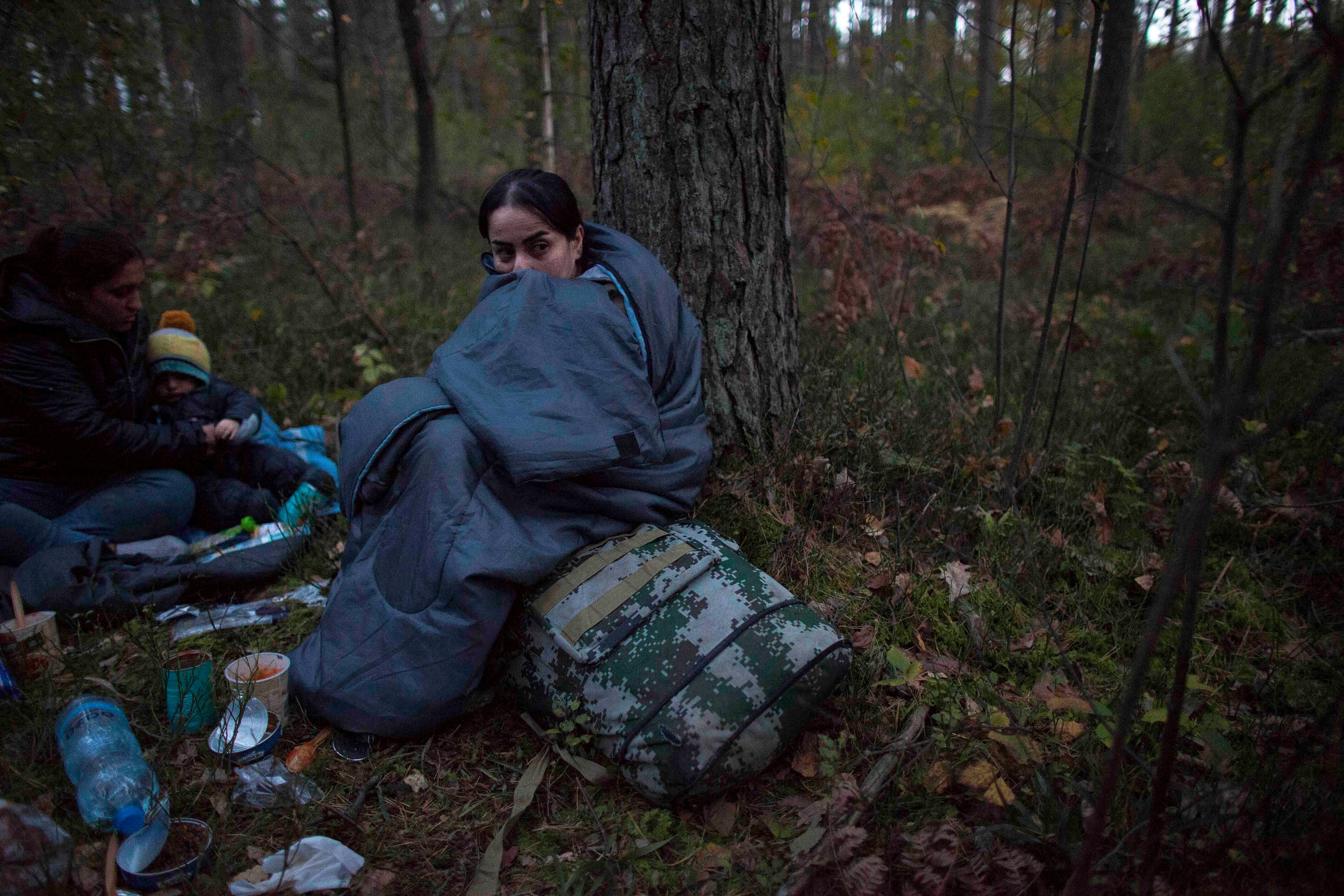 Two women and a child huddle in sleeping bags on the forest floor after crossing the Polish-Belarusian border near Michalowo on October 6, 2021.