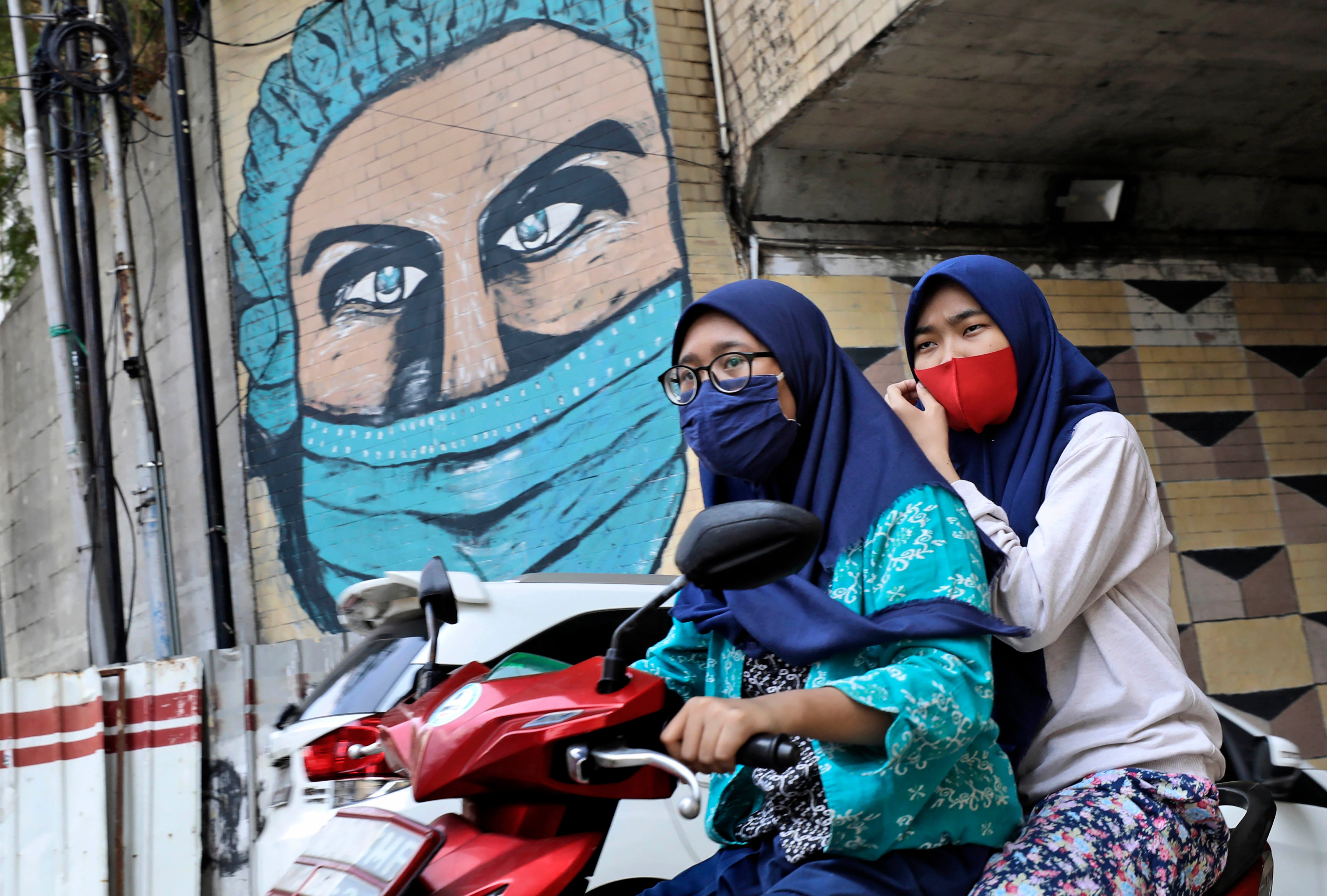 Women ride a motorbike past a large Covid-19-themed mural in Jakarta, Indonesia, October 2, 2020.