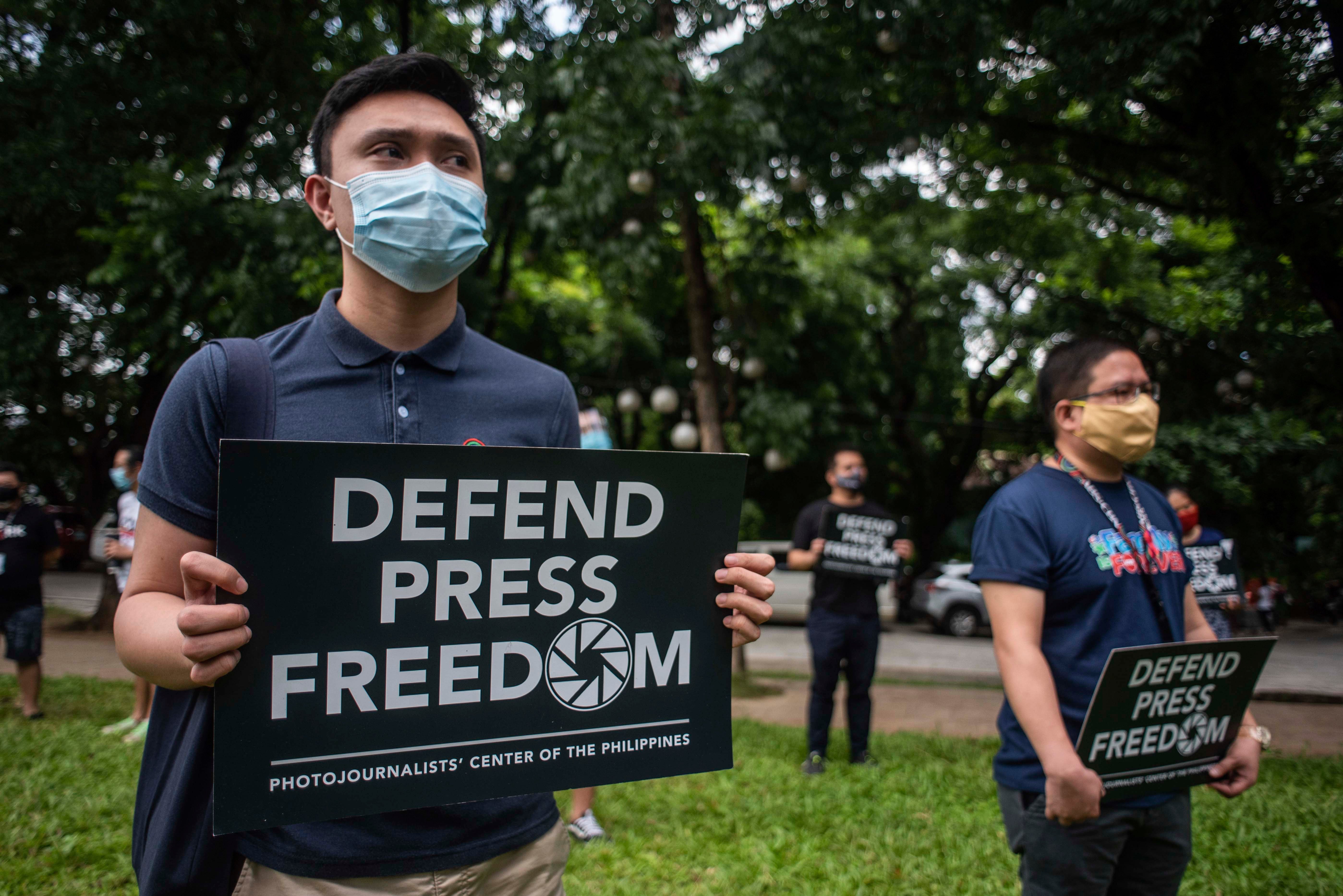 People in face masks hold signs that read "Defend Press Freedom"