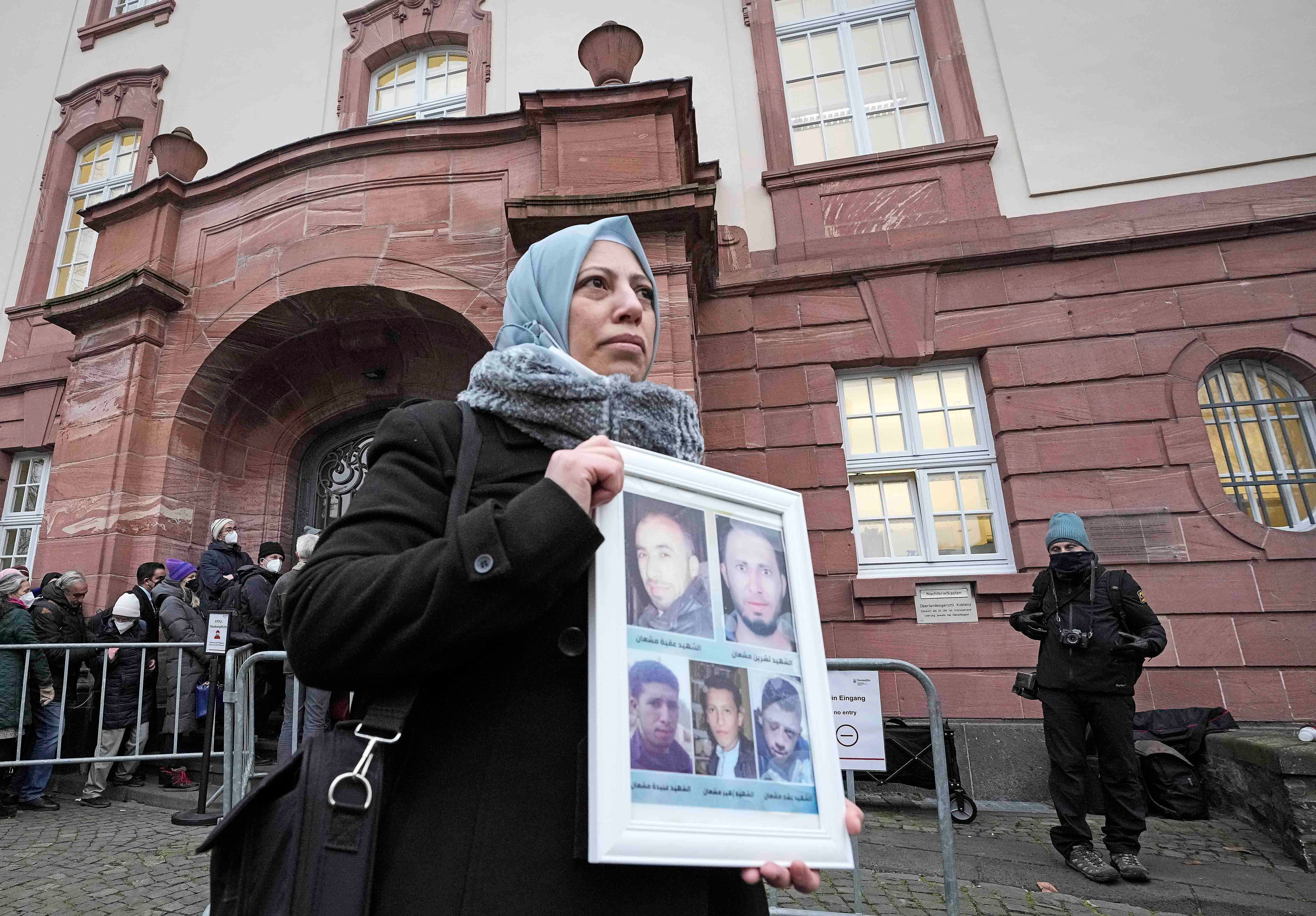 Yasmen Almashan from Syria holds a poster with pictures of her five brothers who died in Syria as she waits in front of the court in Koblenz, Germany