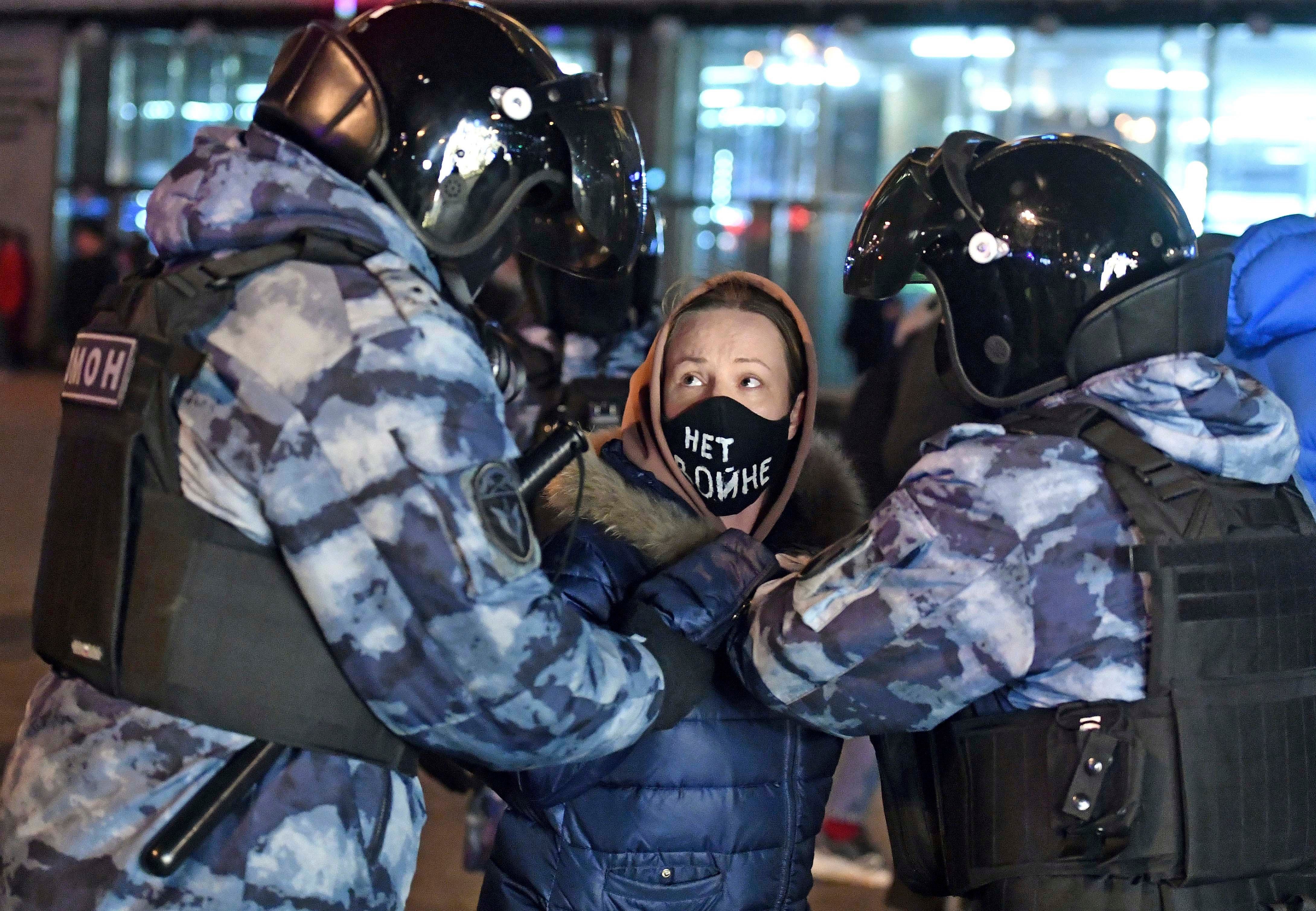 Une jeune manifestante est arrêtée par deux policiers sur la place Pouchkine, à Moscou, le 24 février 2022, lors d’une manifestation contre les opérations militaires de grande ampleur contre l’Ukraine ordonnées par le président Vladimir Poutine. Sur son masque, en lettres blanches, est inscrit le message « Non à la guerre ».