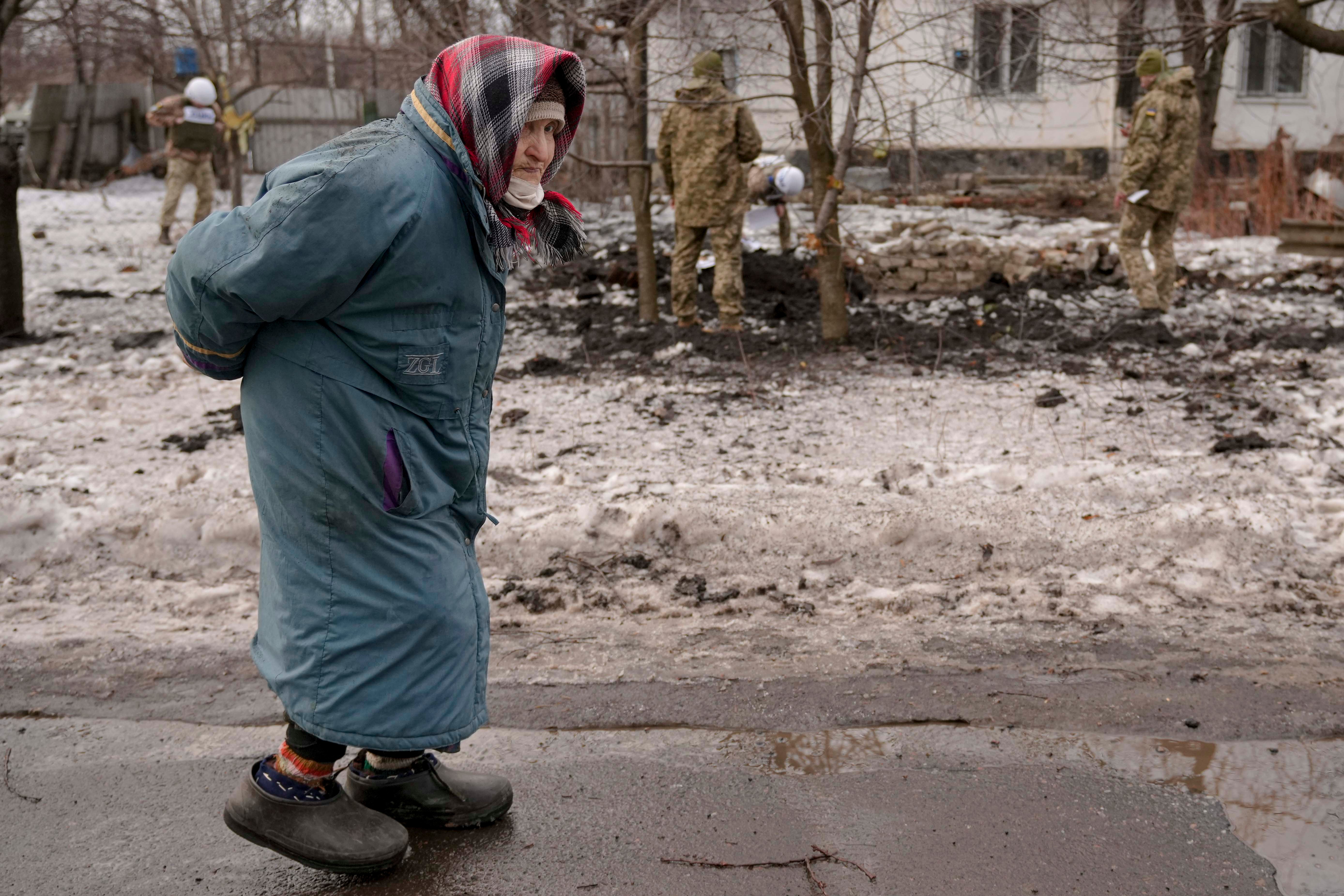 A woman walks near the line of contact, as Ukrainian personnel survey a crater and damage to a house from shelling in Vrubivka, eastern Ukraine, February 17, 2022.
