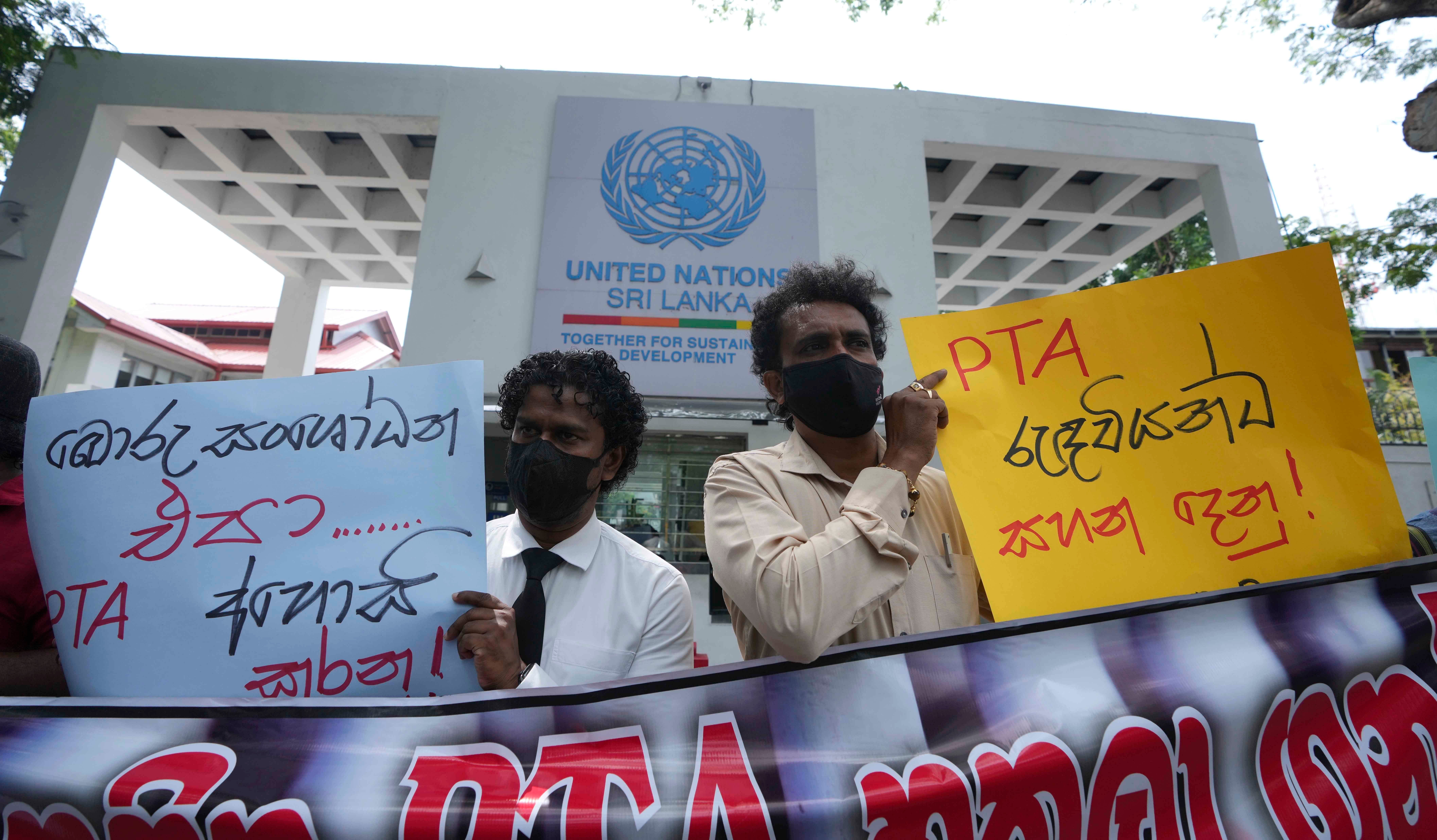 Two people hold protest signs written in Sinhalese 